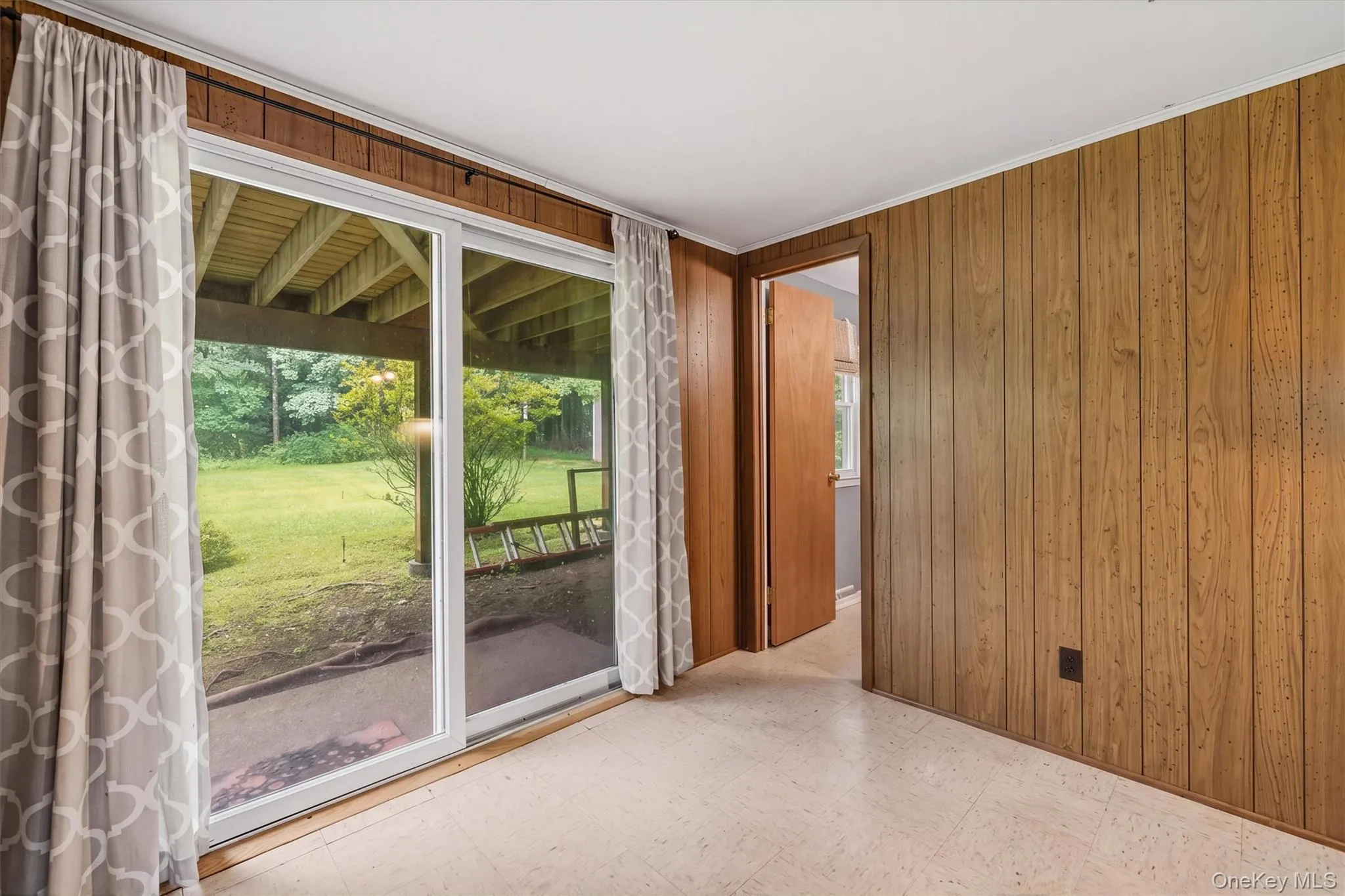 Sliding glass door access to the exterior, wood paneling, and neutral flooring Sliding glass door access to the exterior, wood paneling, and neutral flooring