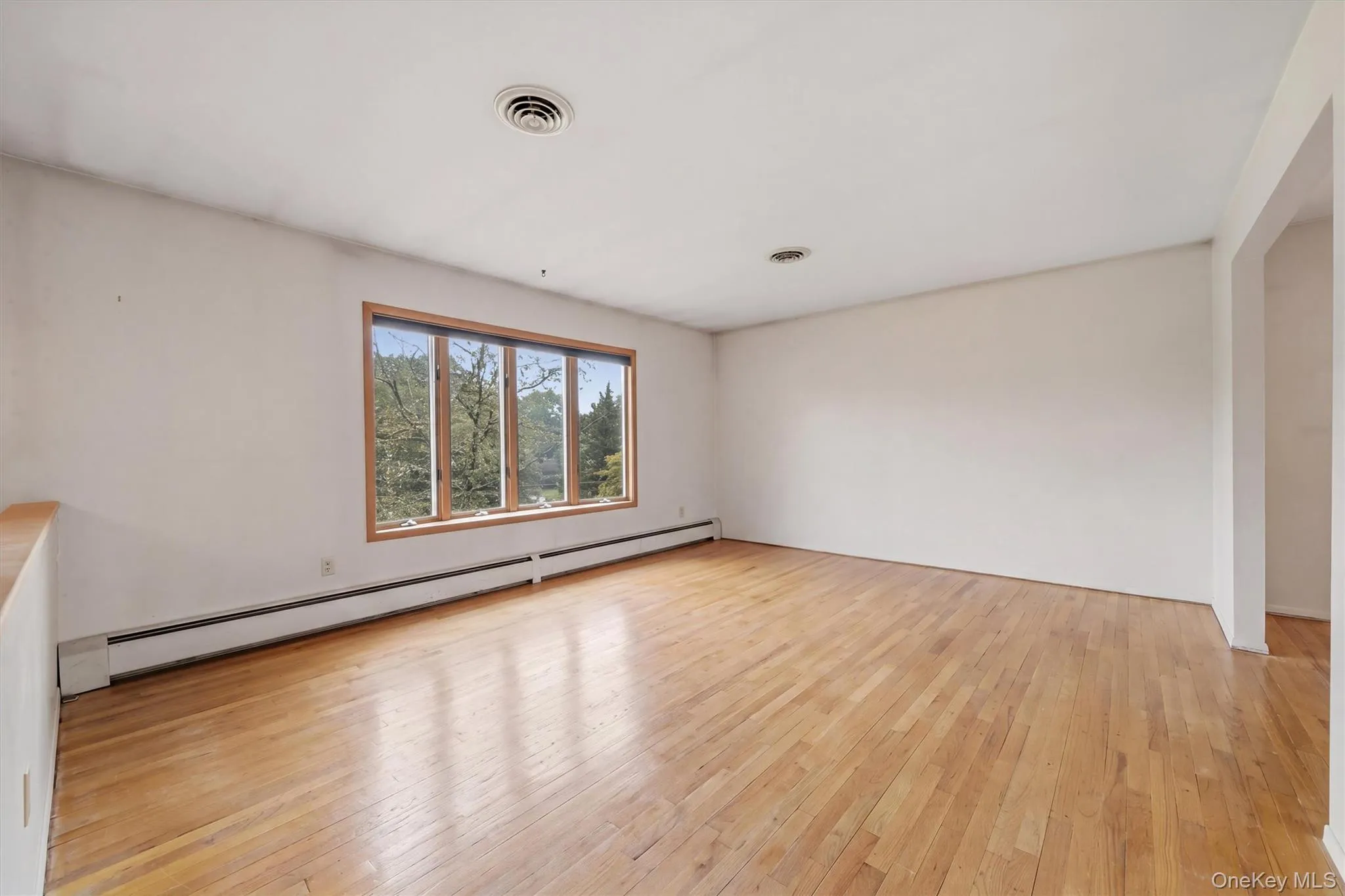 Expansive room featuring wood-finish flooring, a large multi-pane window with wood trim, Expansive room featuring wood-finish flooring, a large multi-pane window with wood trim,