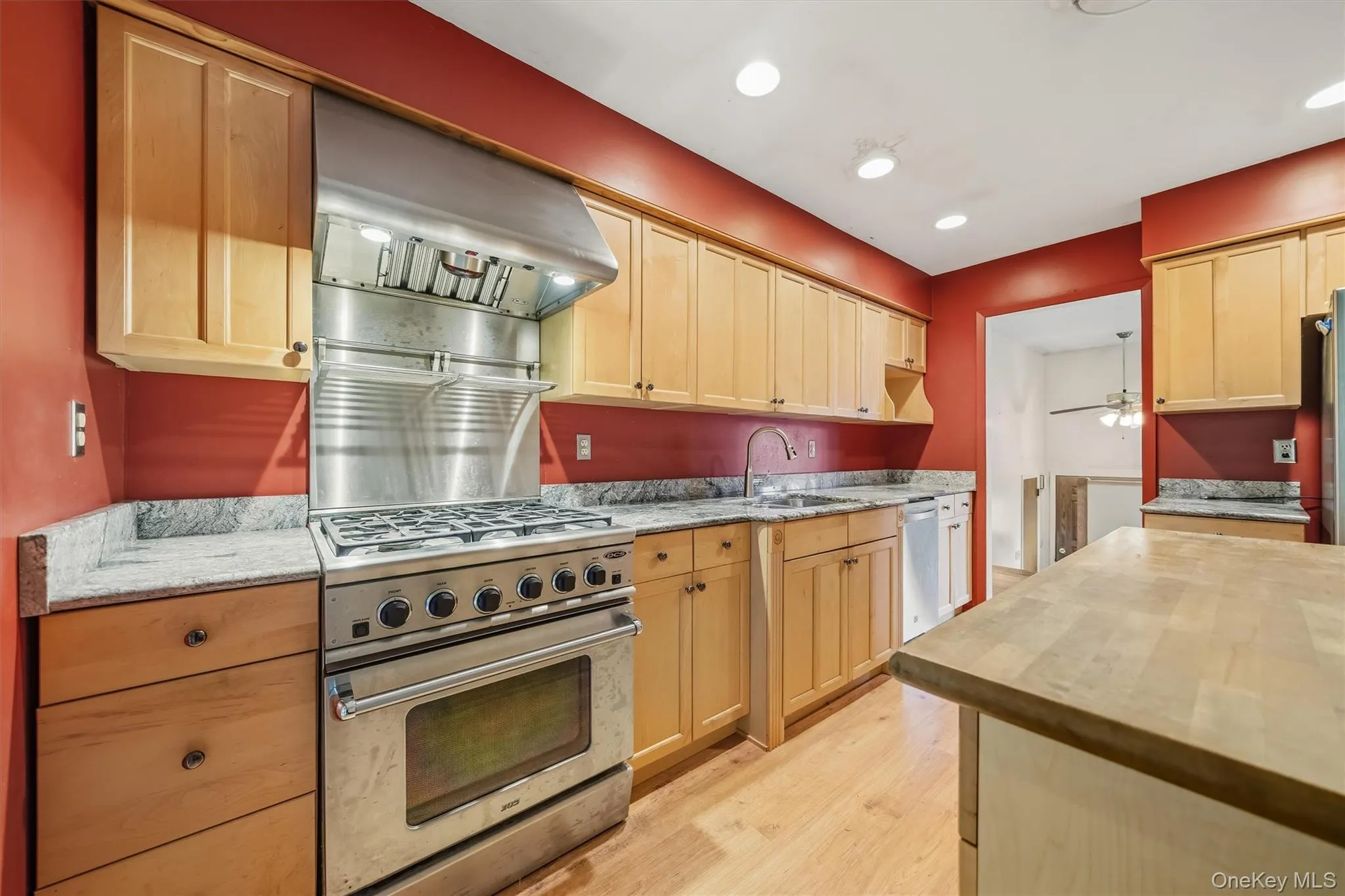 Stainless steel gas range with a matching professional-grade hood, light wood-finish cabinetry, granite countertops, wood-finish flooring, and recessed lighting Stainless steel gas range with a matching professional-grade hood, light wood-finish cabinetry, granite countertops, wood-finish flooring, and recessed lighting