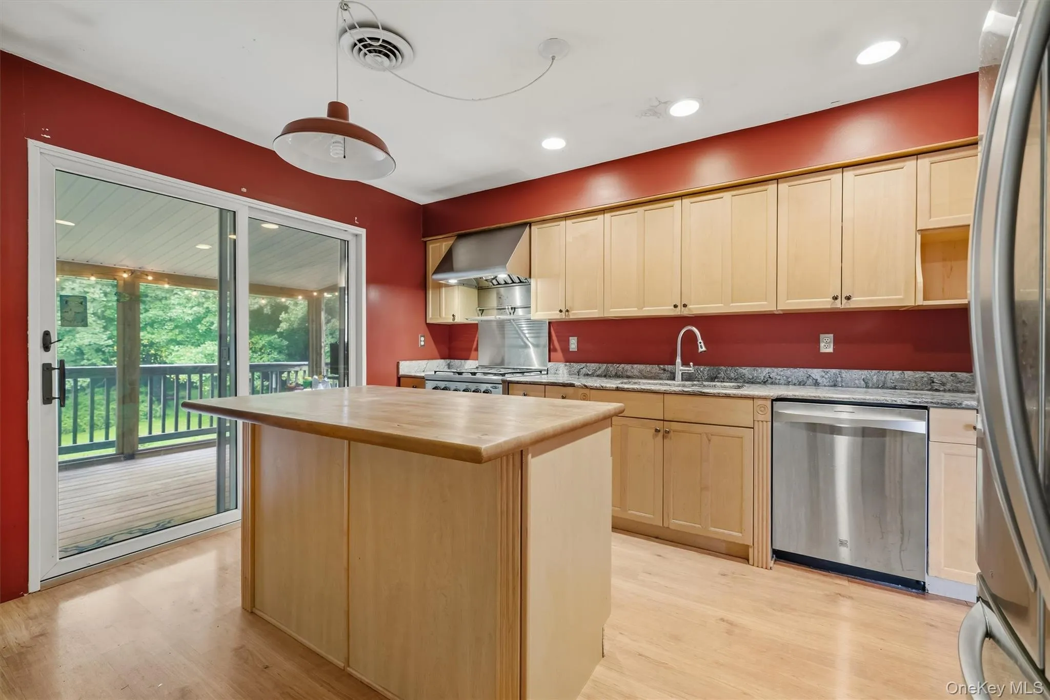 Kitchen featuring wood-finish flooring, light wood cabinetry, granite countertops, stainless steel appliances, and sliding glass door access to an exterior deck Kitchen featuring wood-finish flooring, light wood cabinetry, granite countertops, stainless steel appliances, and sliding glass door access to an exterior deck