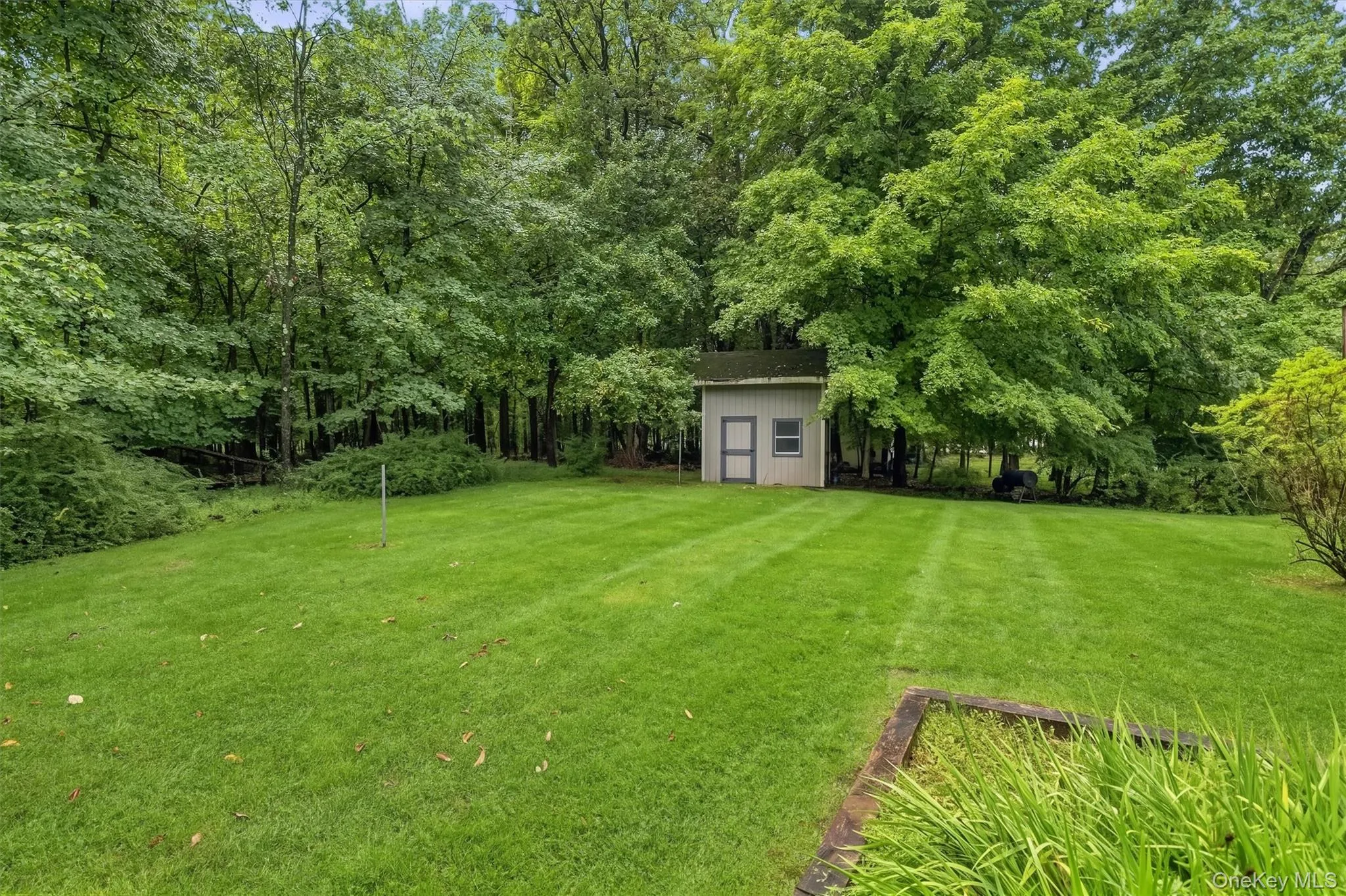 Expansive lawn featuring mature trees, a detached storage shed, and integrated landscaping Expansive lawn featuring mature trees, a detached storage shed, and integrated landscaping