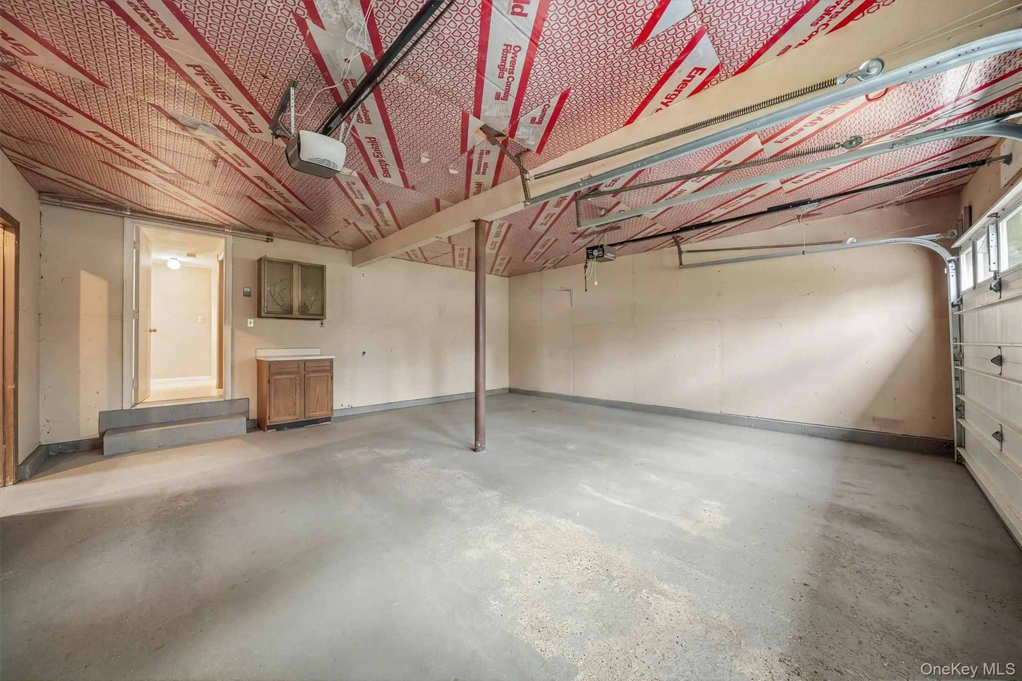 Attached garage with concrete flooring, insulated ceiling, a built-in wood-finish cabinet, and a utility sink Attached garage with concrete flooring, insulated ceiling, a built-in wood-finish cabinet, and a utility sink