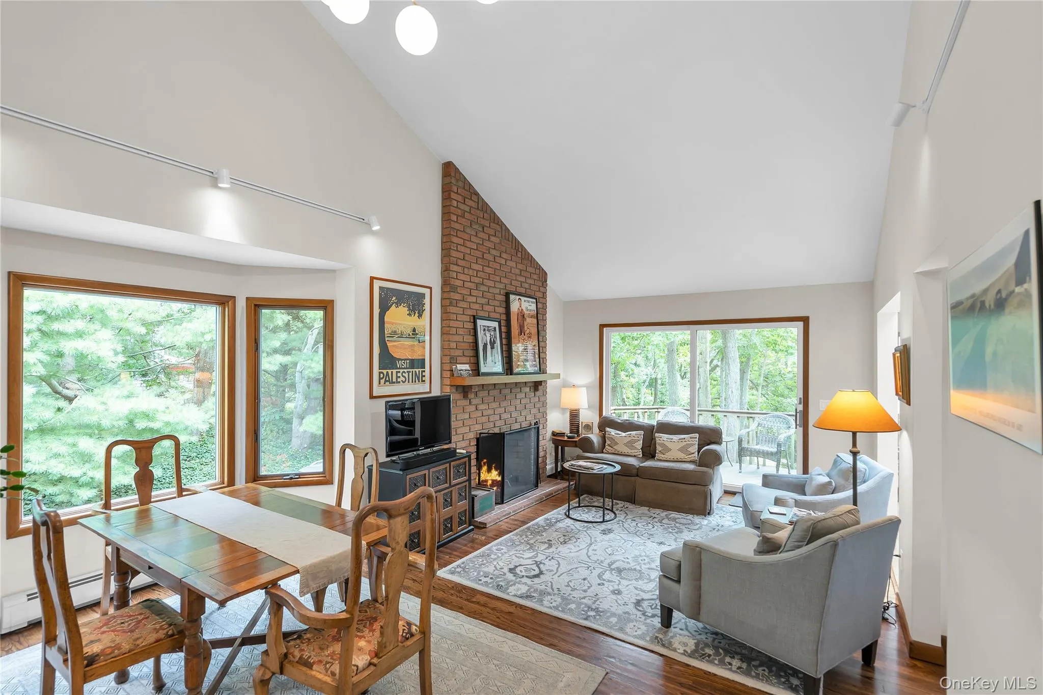 Vaulted ceiling with track lighting, brick fireplace with wood mantel, wood-finish flooring, bay window, and glass sliding doors to deck Vaulted ceiling with track lighting, brick fireplace with wood mantel, wood-finish flooring, bay window, and glass sliding doors to deck