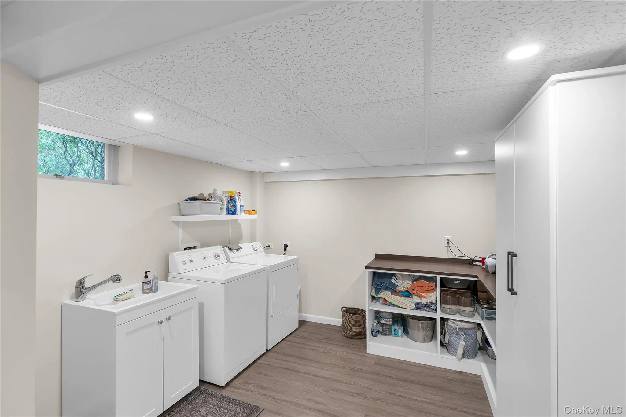 Recessed lighting illuminating the Laundry Room space, wood-finish flooring, white cabinetry with integrated sink, white storage cupboards, and built-in shelving with wood-finish countertop Recessed lighting illuminating the Laundry Room space, wood-finish flooring, white cabinetry with integrated sink, white storage cupboards, and built-in shelving with wood-finish countertop