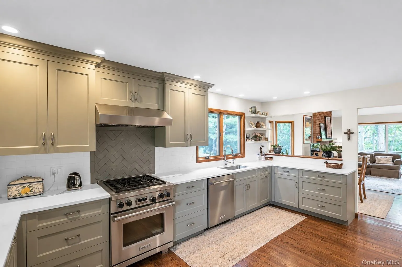Kitchen featuring new sage shaker cabinetry, stainless steel appliances, Wolf stove, quartz countertops, a gray herringbone tile backsplash, and wood-finish flooring Kitchen featuring new sage shaker cabinetry, stainless steel appliances, Wolf stove, quartz countertops, a gray herringbone tile backsplash, and wood-finish flooring