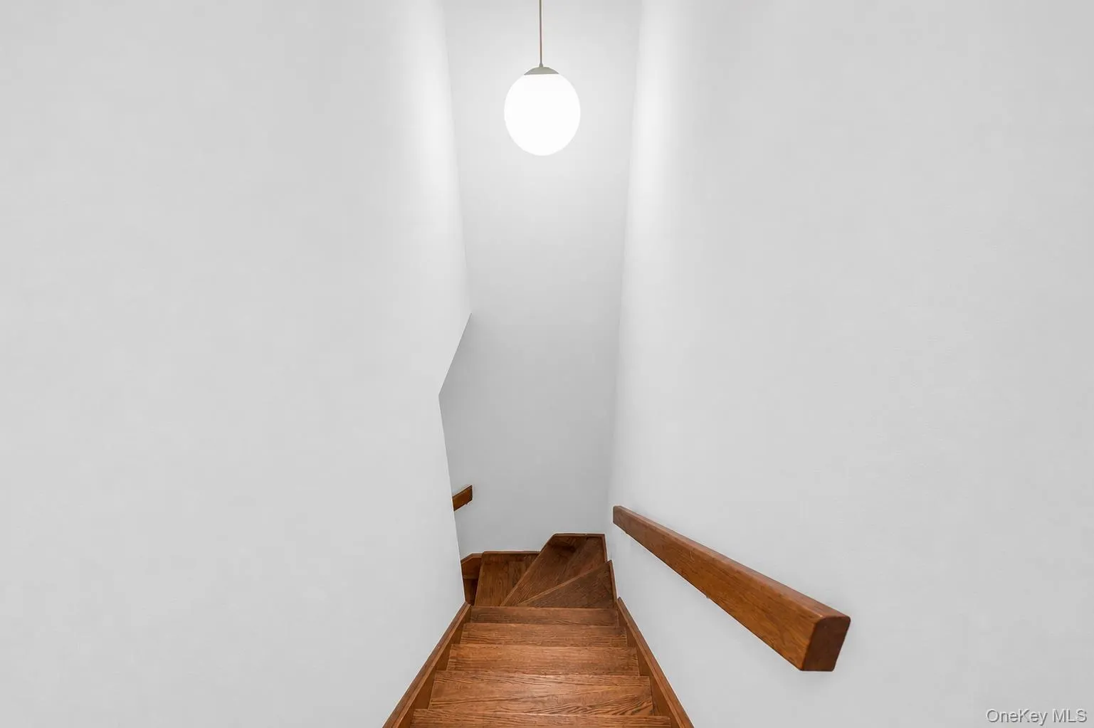 Wood-finish staircase with solid wood handrails and a spherical pendant light fixture leading to upstairs bedrooms Wood-finish staircase with solid wood handrails and a spherical pendant light fixture leading to upstairs bedrooms
