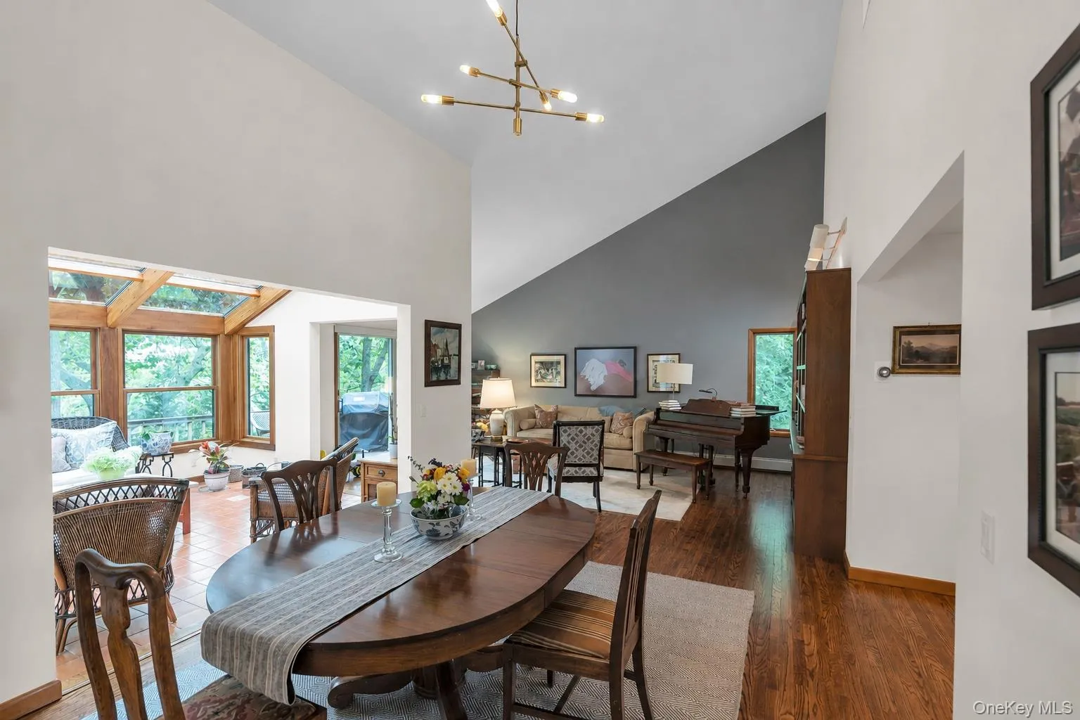 Open Dining Room area with multiple windows, vaulted ceilings, wood-finish flooring, and a modern linear chandelier Open Dining Room area with multiple windows, vaulted ceilings, wood-finish flooring, and a modern linear chandelier