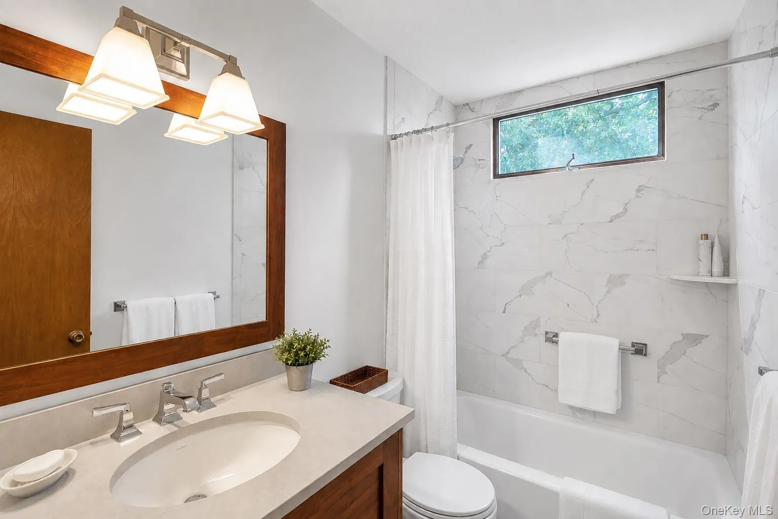 Second Floor Full Bathroom featuring a wood-framed mirror, vanity with an under mount sink, marble-look tile shower surround, and a clerestory window Second Floor Full Bathroom featuring a wood-framed mirror, vanity with an under mount sink, marble-look tile shower surround, and a clerestory window