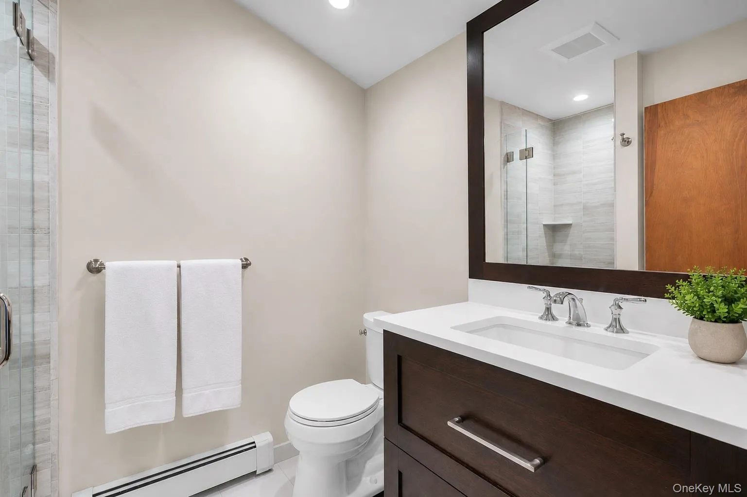 Primary Ensuite Full Bathroom. Dark wood-finish vanity with an integrated sink and white countertop, framed mirror, and glass-enclosed shower with tiled walls Primary Ensuite Full Bathroom. Dark wood-finish vanity with an integrated sink and white countertop, framed mirror, and glass-enclosed shower with tiled walls