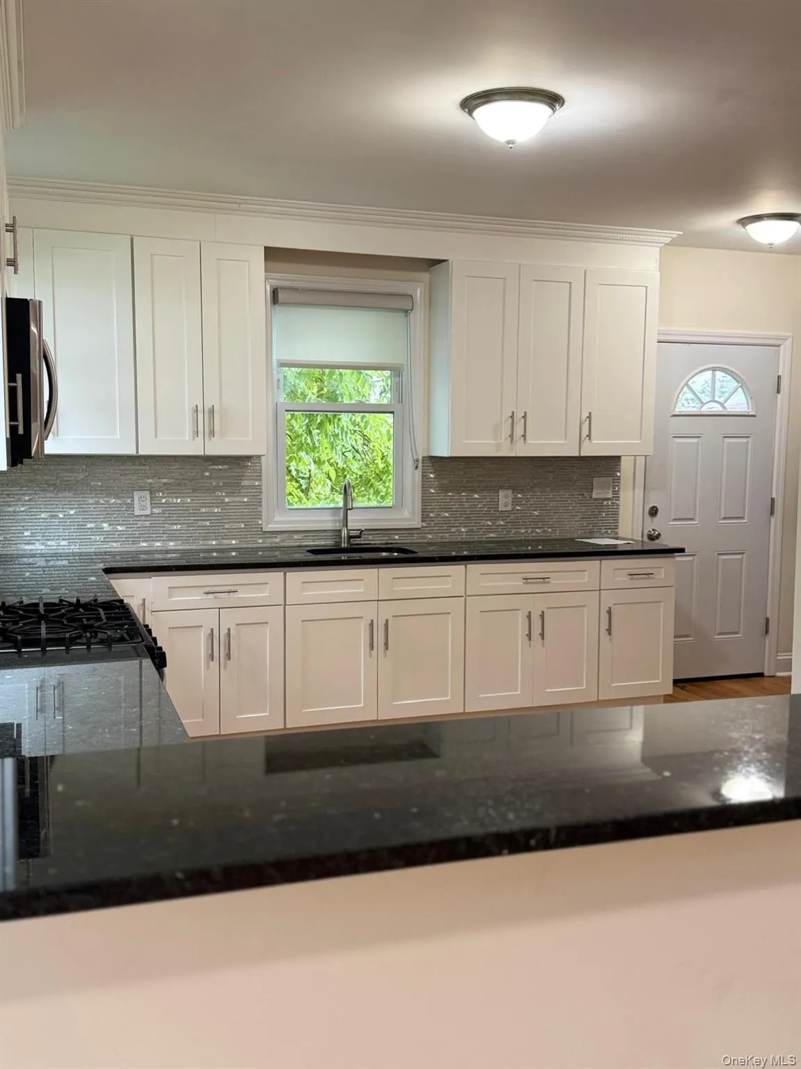 White shaker-style cabinetry with dark countertops, a tile backsplash, and stainless steel hardware White shaker-style cabinetry with dark countertops, a tile backsplash, and stainless steel hardware