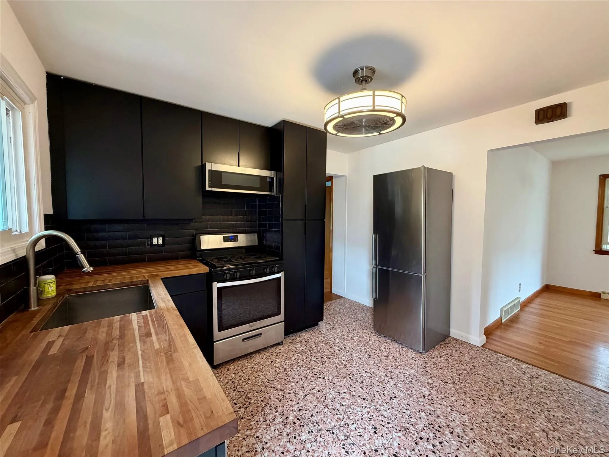 Kitchen featuring black cabinetry, stainless steel appliances, wood-finish countertops, black subway tile backsplash, and a patterned floor Kitchen featuring black cabinetry, stainless steel appliances, wood-finish countertops, black subway tile backsplash, and a patterned floor