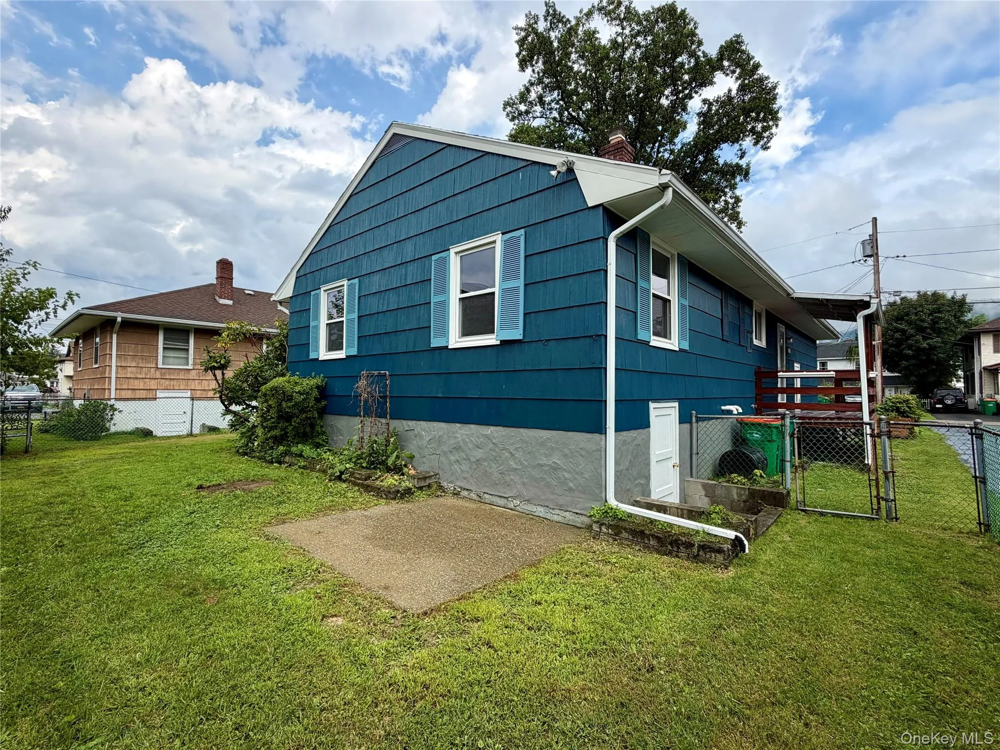 Charming blue cottage featuring a gabled roofline with dual front-facing windows, elevated foundation, and a spacious lawn with mature landscaping Charming blue cottage featuring a gabled roofline with dual front-facing windows, elevated foundation, and a spacious lawn with mature landscaping
