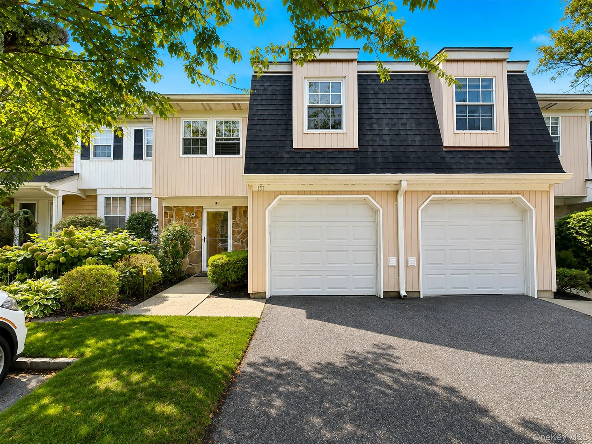 Car garage with white paneled doors, dormer windows, natural stone façade accents, and a paved driveway Car garage with white paneled doors, dormer windows, natural stone façade accents, and a paved driveway