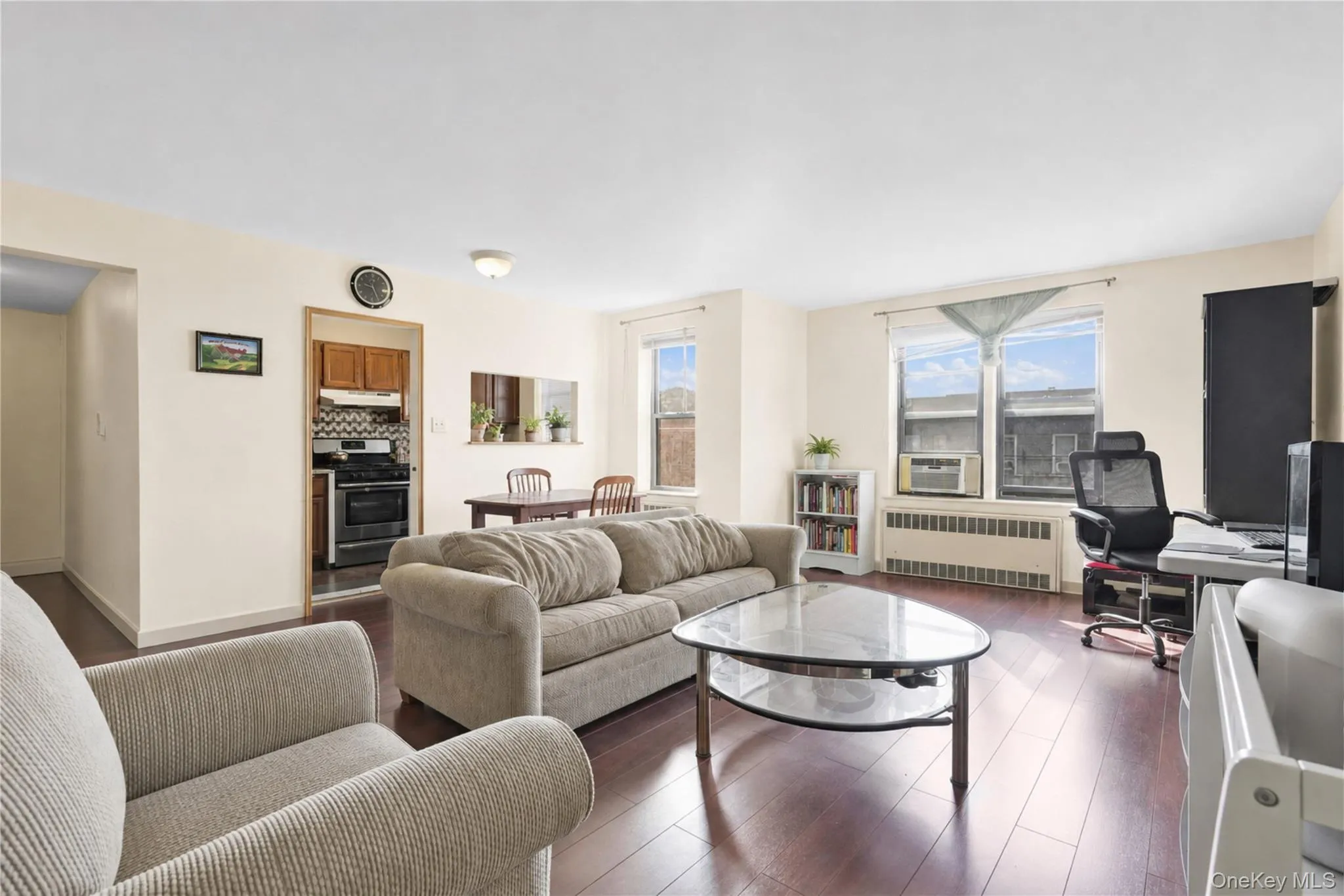 Dark wood-finish flooring throughout, multiple windows, built-in wall unit, and a pass-through opening to the kitchen Dark wood-finish flooring throughout, multiple windows, built-in wall unit, and a pass-through opening to the kitchen