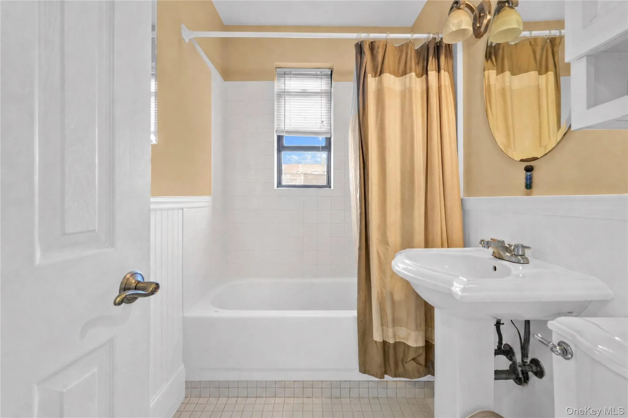 Bathroom featuring a pedestal sink, white tile flooring, and wainscoting Bathroom featuring a pedestal sink, white tile flooring, and wainscoting