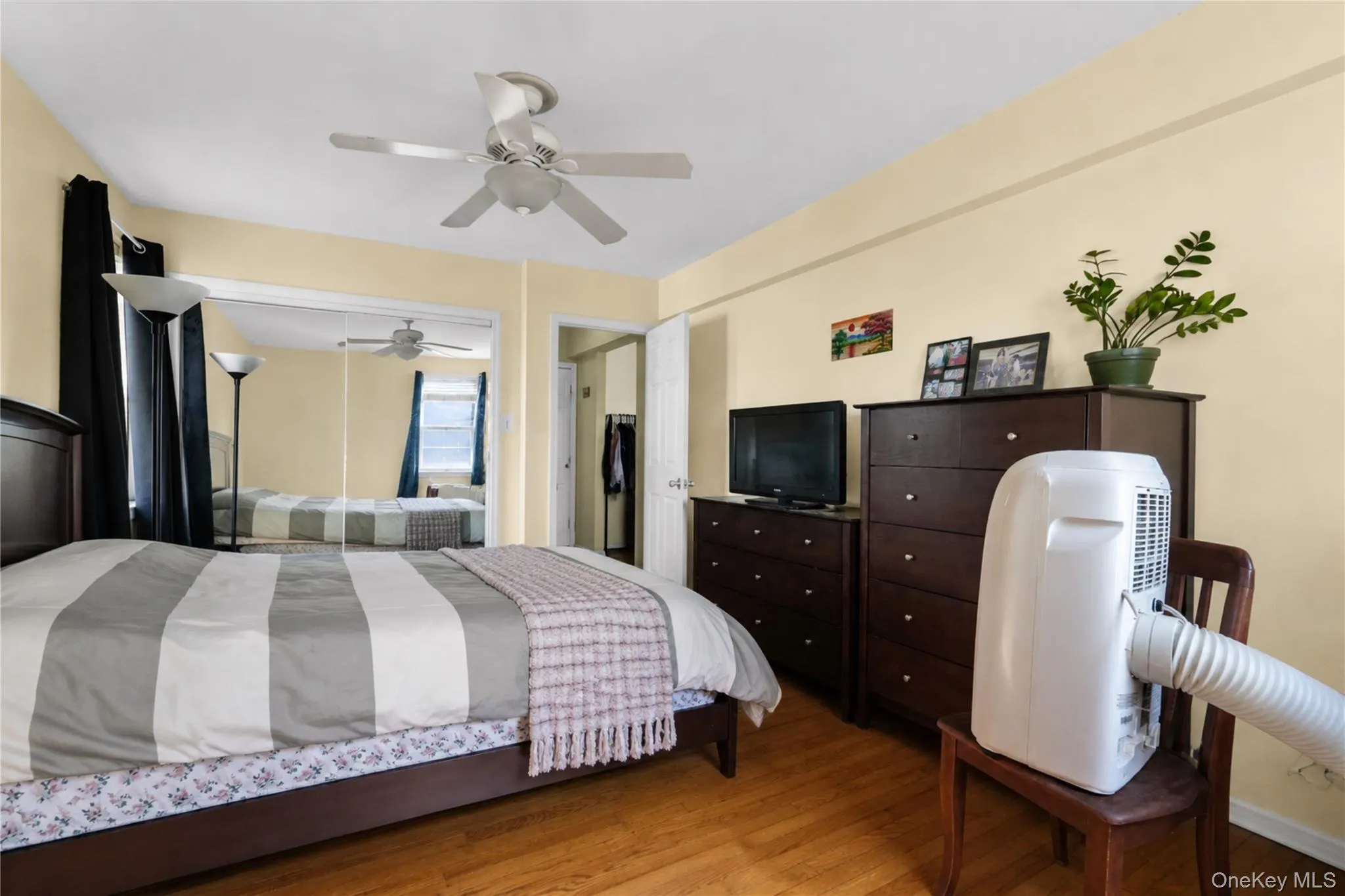 Hardwood flooring, mirrored closet doors, ceiling fan with light fixture, and a built-in closet with shelving Hardwood flooring, mirrored closet doors, ceiling fan with light fixture, and a built-in closet with shelving