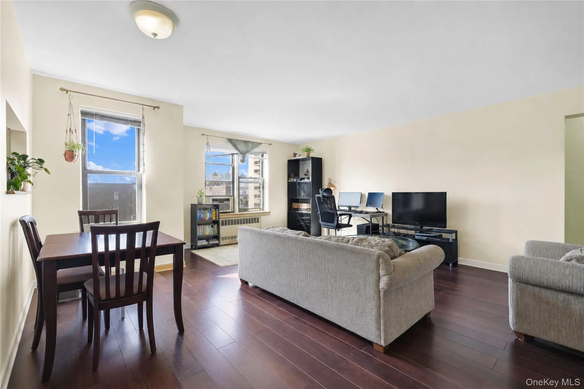 Expansive open-concept living space with dark wood-finish flooring, light-toned wall paint, and multiple windows providing natural illumination Expansive open-concept living space with dark wood-finish flooring, light-toned wall paint, and multiple windows providing natural illumination