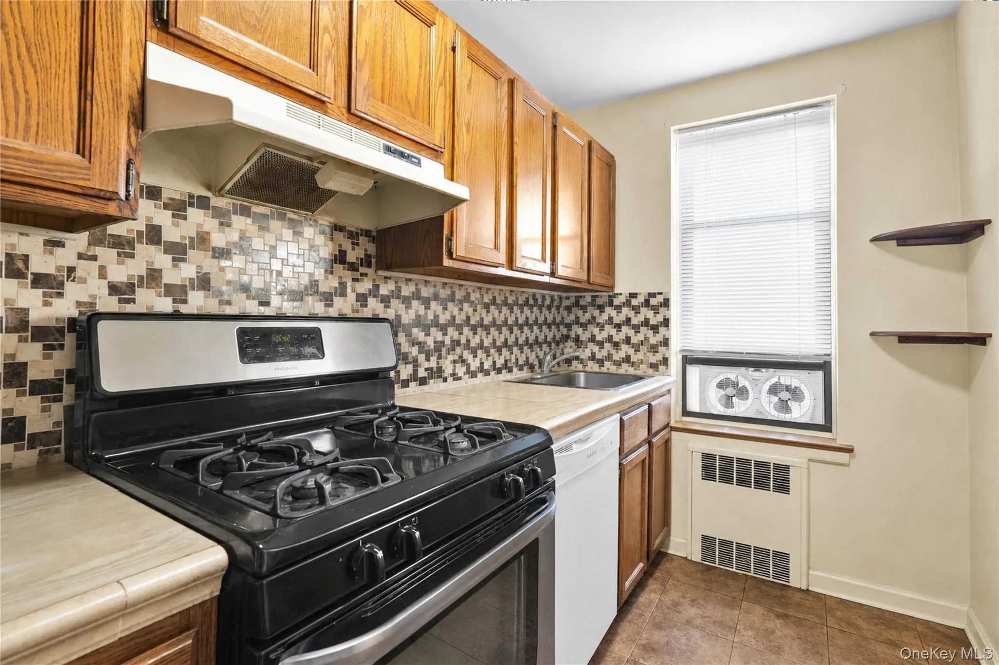 Kitchen featuring wood-finish cabinetry, mosaic tile backsplash, countertop space, a built-in oven with a cooktop, and a window Kitchen featuring wood-finish cabinetry, mosaic tile backsplash, countertop space, a built-in oven with a cooktop, and a window