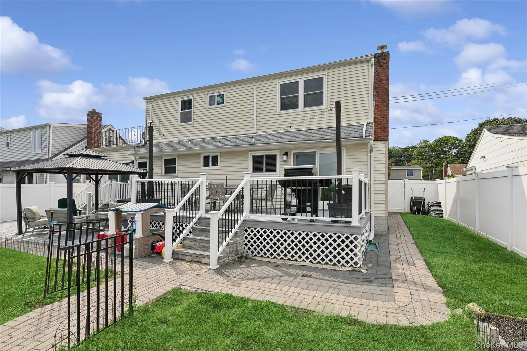 Rear exterior featuring siding, brick chimney, elevated deck with railing, and a paver patio with a gazebo Rear exterior featuring siding, brick chimney, elevated deck with railing, and a paver patio with a gazebo