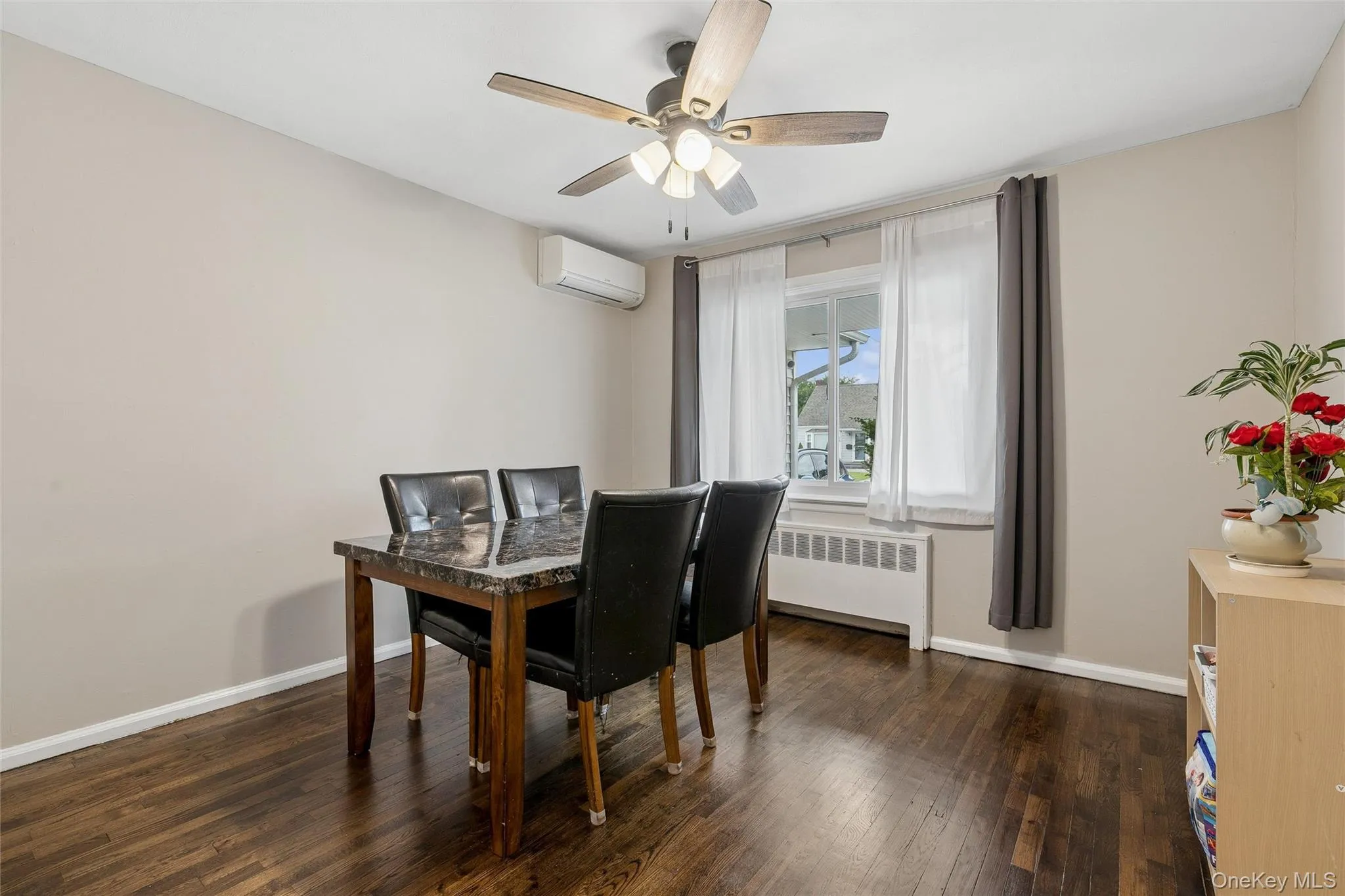 Hardwood flooring, ceiling fan with integrated lighting, window with radiator below, and wall-mounted climate control unit Hardwood flooring, ceiling fan with integrated lighting, window with radiator below, and wall-mounted climate control unit