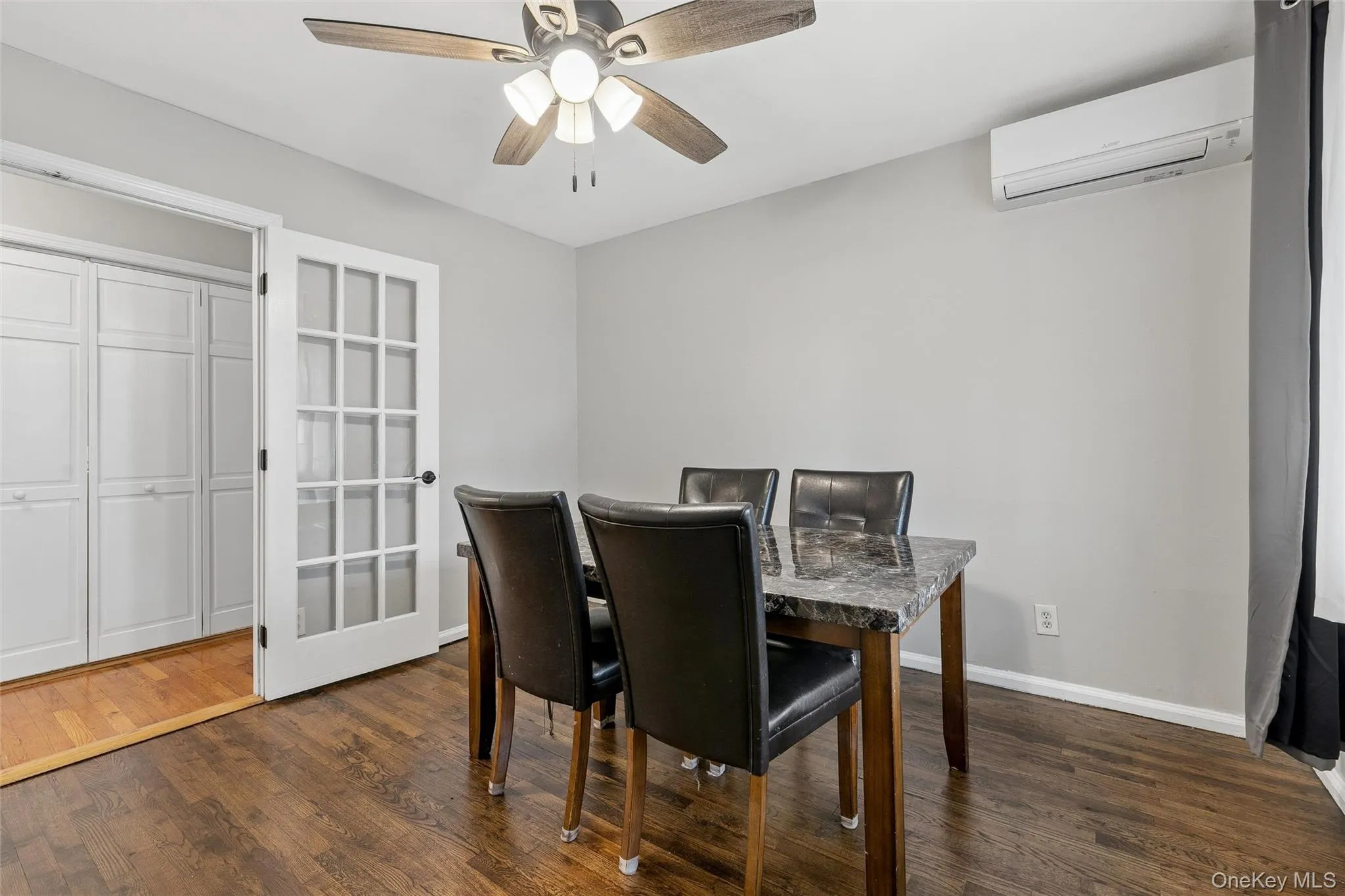 Wood-finish flooring, ceiling fan, French doors with frosted glass, built-in bi-fold closet, and wall-mounted air conditioning unit Wood-finish flooring, ceiling fan, French doors with frosted glass, built-in bi-fold closet, and wall-mounted air conditioning unit