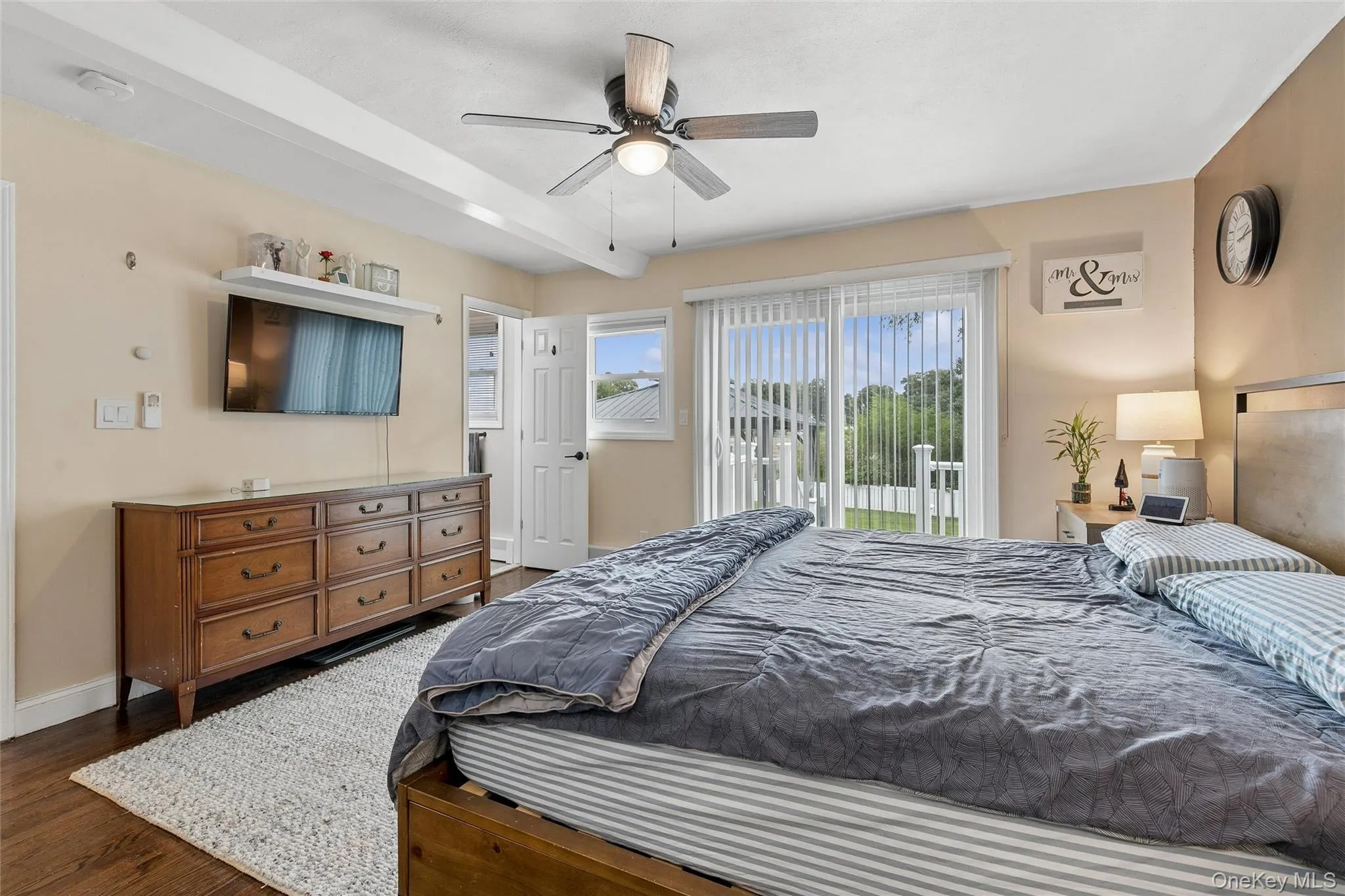 Wood-finish flooring, ceiling fan with integrated lighting, exposed ceiling beam, and sliding glass door with vertical blinds Wood-finish flooring, ceiling fan with integrated lighting, exposed ceiling beam, and sliding glass door with vertical blinds