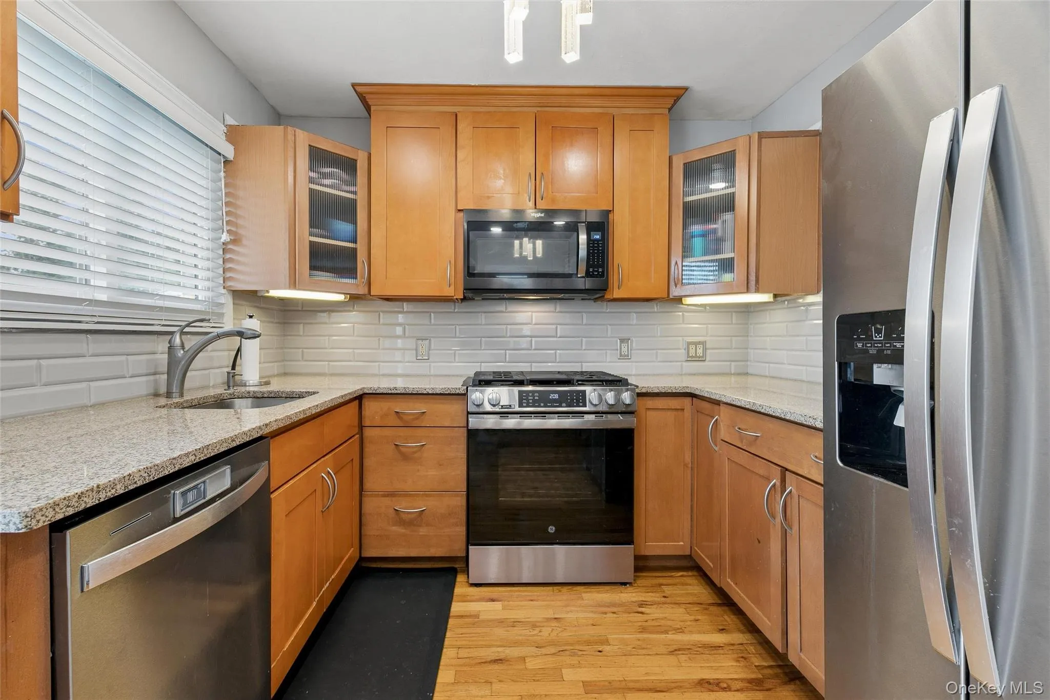 Kitchen featuring natural wood cabinetry, stainless steel appliances, light-toned countertops, and a white subway tile backsplash Kitchen featuring natural wood cabinetry, stainless steel appliances, light-toned countertops, and a white subway tile backsplash