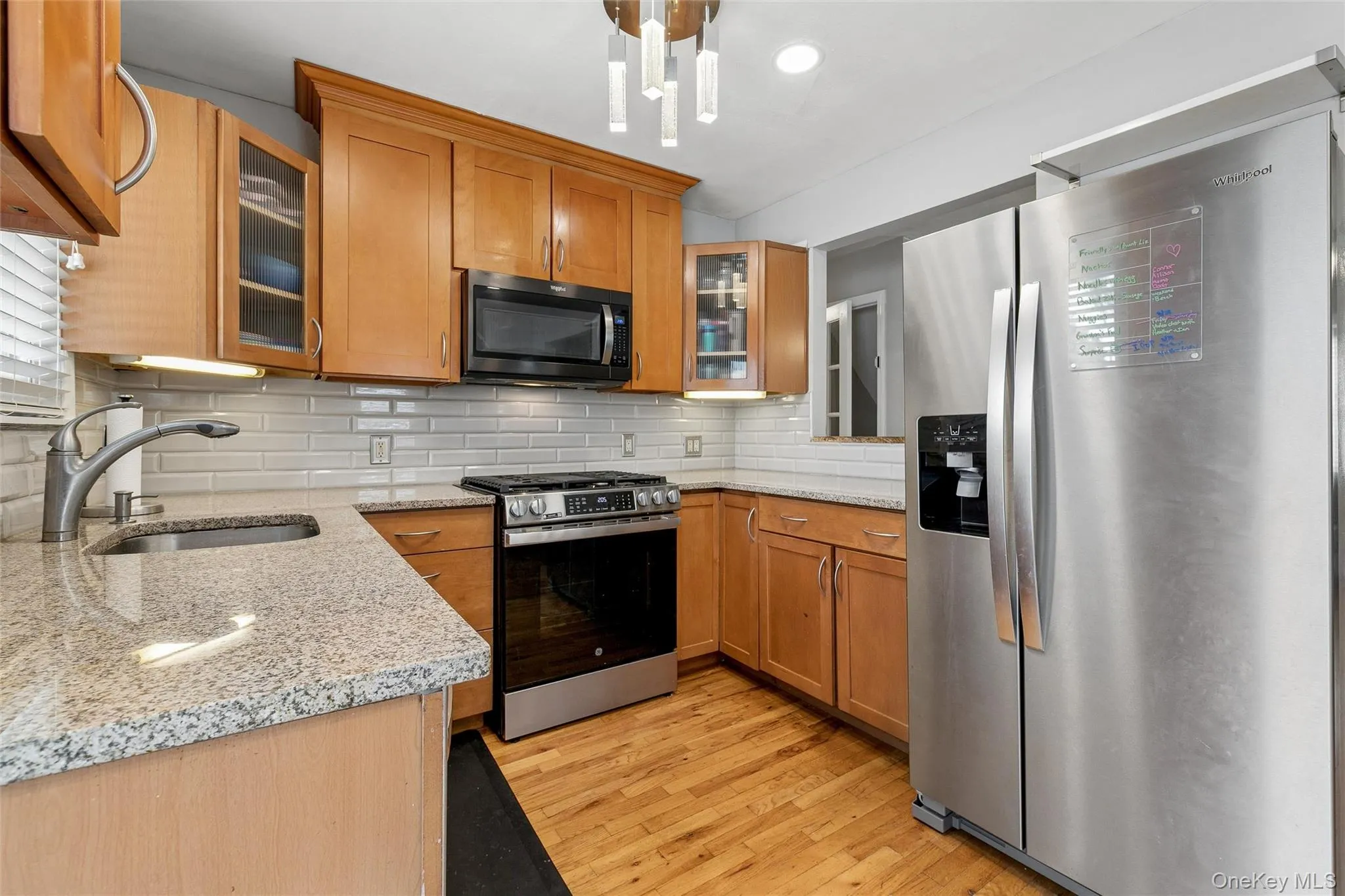 Wood-finish flooring, light wood cabinetry, white subway tile backsplash, granite countertops, and stainless steel appliances Wood-finish flooring, light wood cabinetry, white subway tile backsplash, granite countertops, and stainless steel appliances