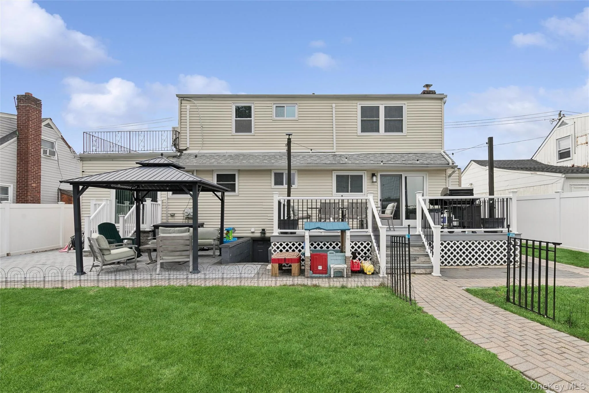 Expansive backyard featuring a manicured lawn, brick paver walkway, and a spacious deck with railing Expansive backyard featuring a manicured lawn, brick paver walkway, and a spacious deck with railing