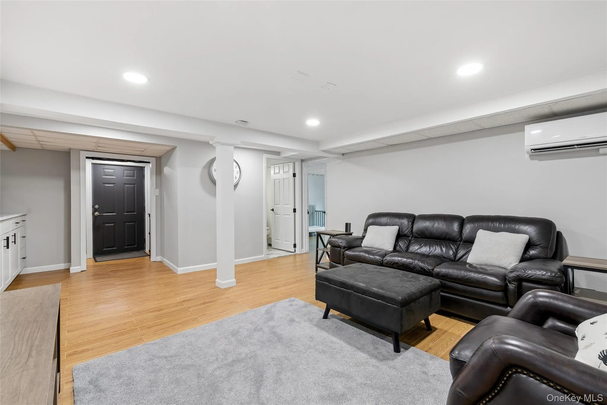 Recessed ceiling lighting, wood-finish flooring, white built-in cabinetry, white interior doors, and a wall-mounted climate control unit Recessed ceiling lighting, wood-finish flooring, white built-in cabinetry, white interior doors, and a wall-mounted climate control unit