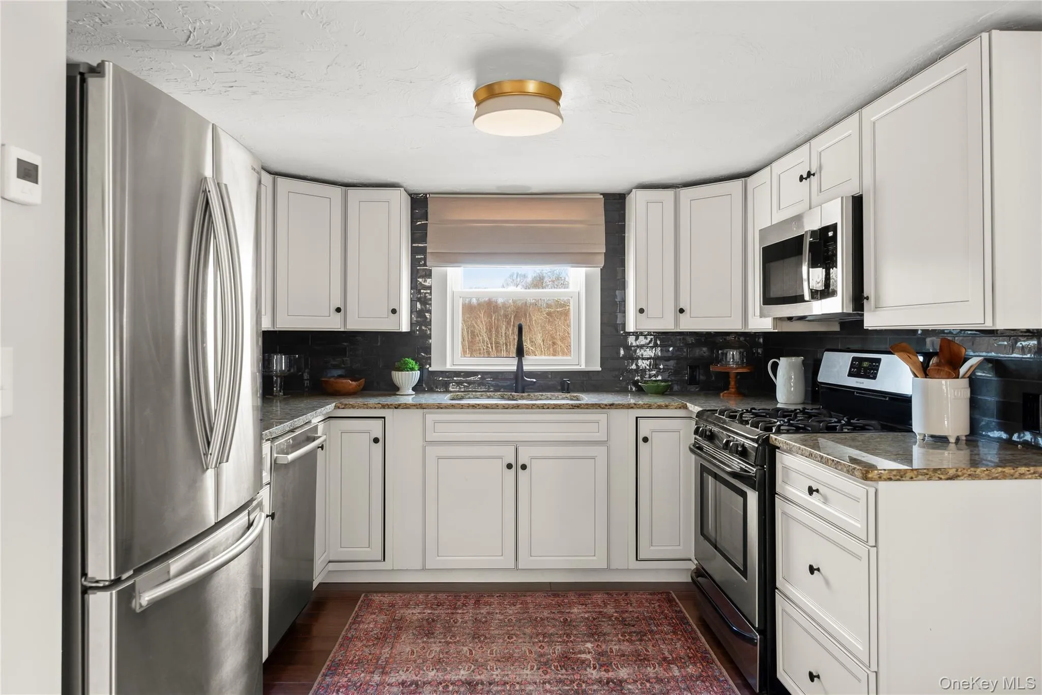 Kitchen with granite countertops, white cabinetry, a sink, backsplash, and appliances with stainless steel finishes Kitchen with granite countertops, white cabinetry, a sink, backsplash, and appliances with stainless steel finishes