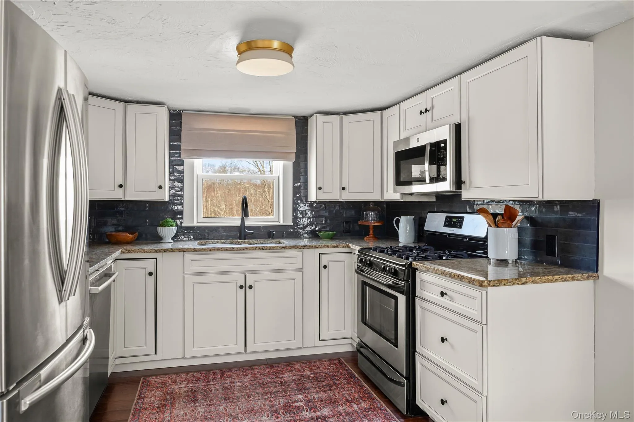 Kitchen with granite countertops, white cabinetry, a sink, appliances with stainless steel finishes, and backsplash Kitchen with granite countertops, white cabinetry, a sink, appliances with stainless steel finishes, and backsplash