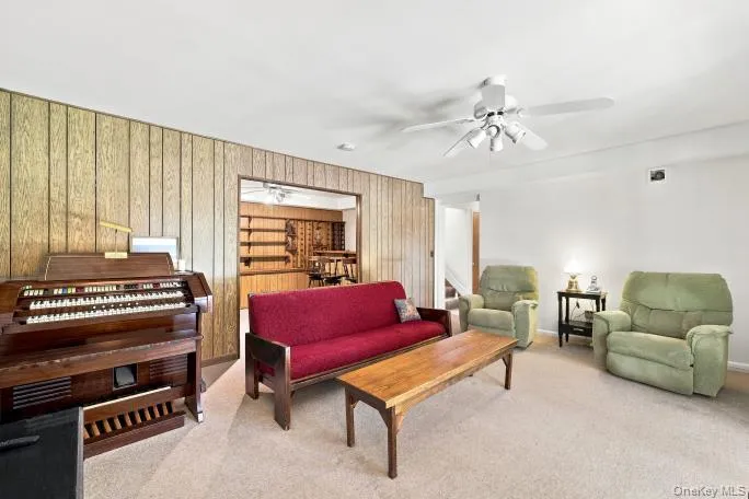 Carpeted flooring, paneled accent wall, overhead ceiling fan with lighting, and an open doorway reveal an additional space with wood shelving Carpeted flooring, paneled accent wall, overhead ceiling fan with lighting, and an open doorway reveal an additional space with wood shelving
