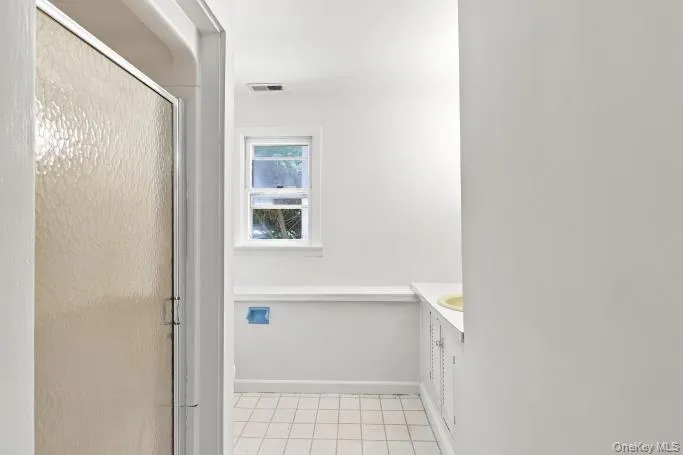 Frosted glass shower enclosure, single window, white tiled flooring, built-in shelving, and white vanity cabinetry Frosted glass shower enclosure, single window, white tiled flooring, built-in shelving, and white vanity cabinetry