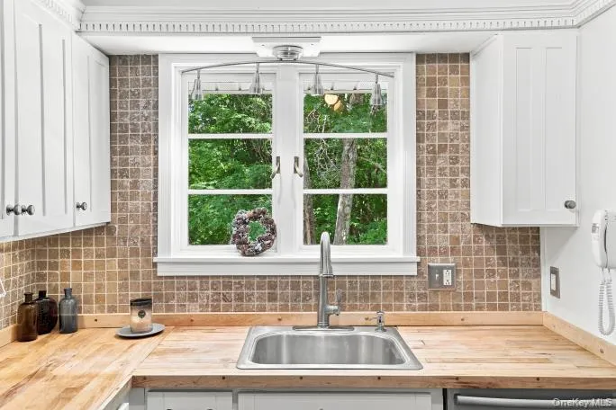 White shaker-style cabinetry, wood-finish countertops, stainless steel sink with a gooseneck faucet, and mosaic tile backsplash White shaker-style cabinetry, wood-finish countertops, stainless steel sink with a gooseneck faucet, and mosaic tile backsplash