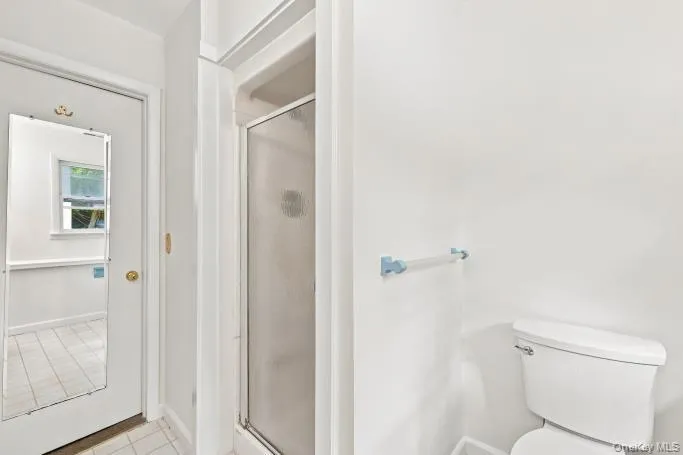 White ceramic tile flooring, enclosed shower with frosted glass door, white toilet, and towel bar White ceramic tile flooring, enclosed shower with frosted glass door, white toilet, and towel bar