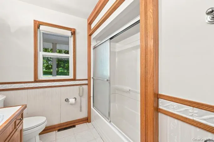 White tiled flooring with a toilet, wood-finish vanity, and a shower with sliding glass doors White tiled flooring with a toilet, wood-finish vanity, and a shower with sliding glass doors