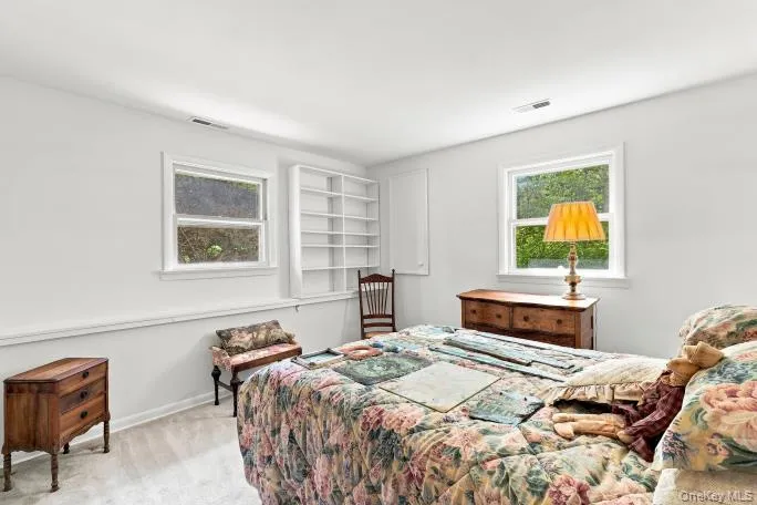 Light-filled room featuring two windows, built-in shelving, and wood-finish flooring Light-filled room featuring two windows, built-in shelving, and wood-finish flooring