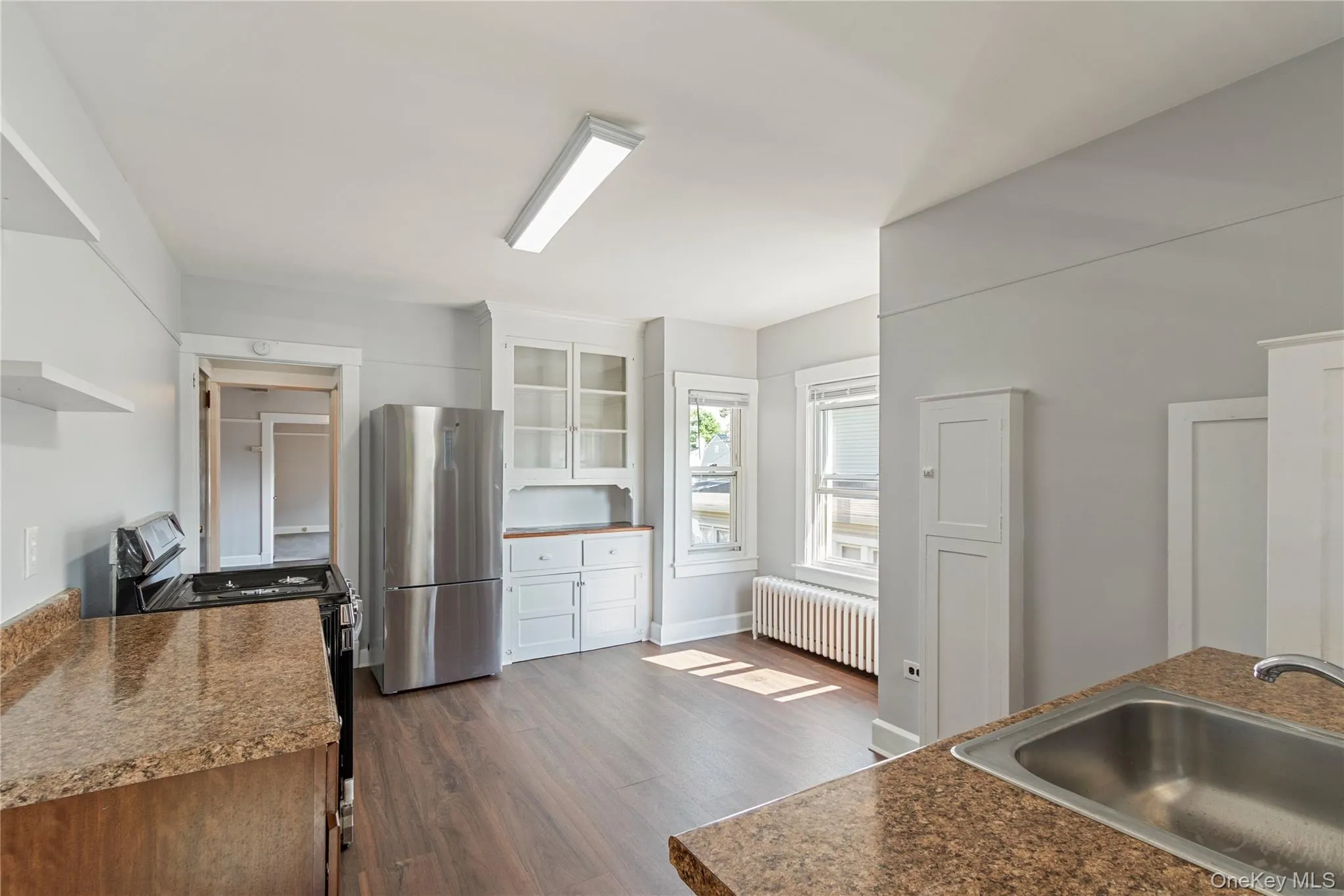 Kitchen featuring wood-finish flooring, white cabinetry, stainless steel refrigerator, and a built-in sink with a granite-look countertop Kitchen featuring wood-finish flooring, white cabinetry, stainless steel refrigerator, and a built-in sink with a granite-look countertop