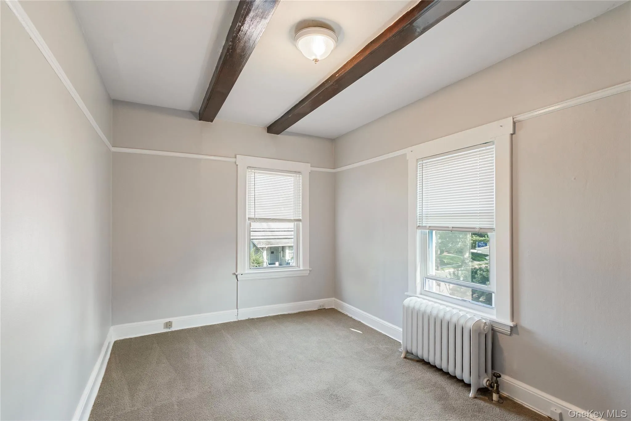 Exposed ceiling beams, two windows, carpeted flooring, and a ceiling-mounted light fixture Exposed ceiling beams, two windows, carpeted flooring, and a ceiling-mounted light fixture