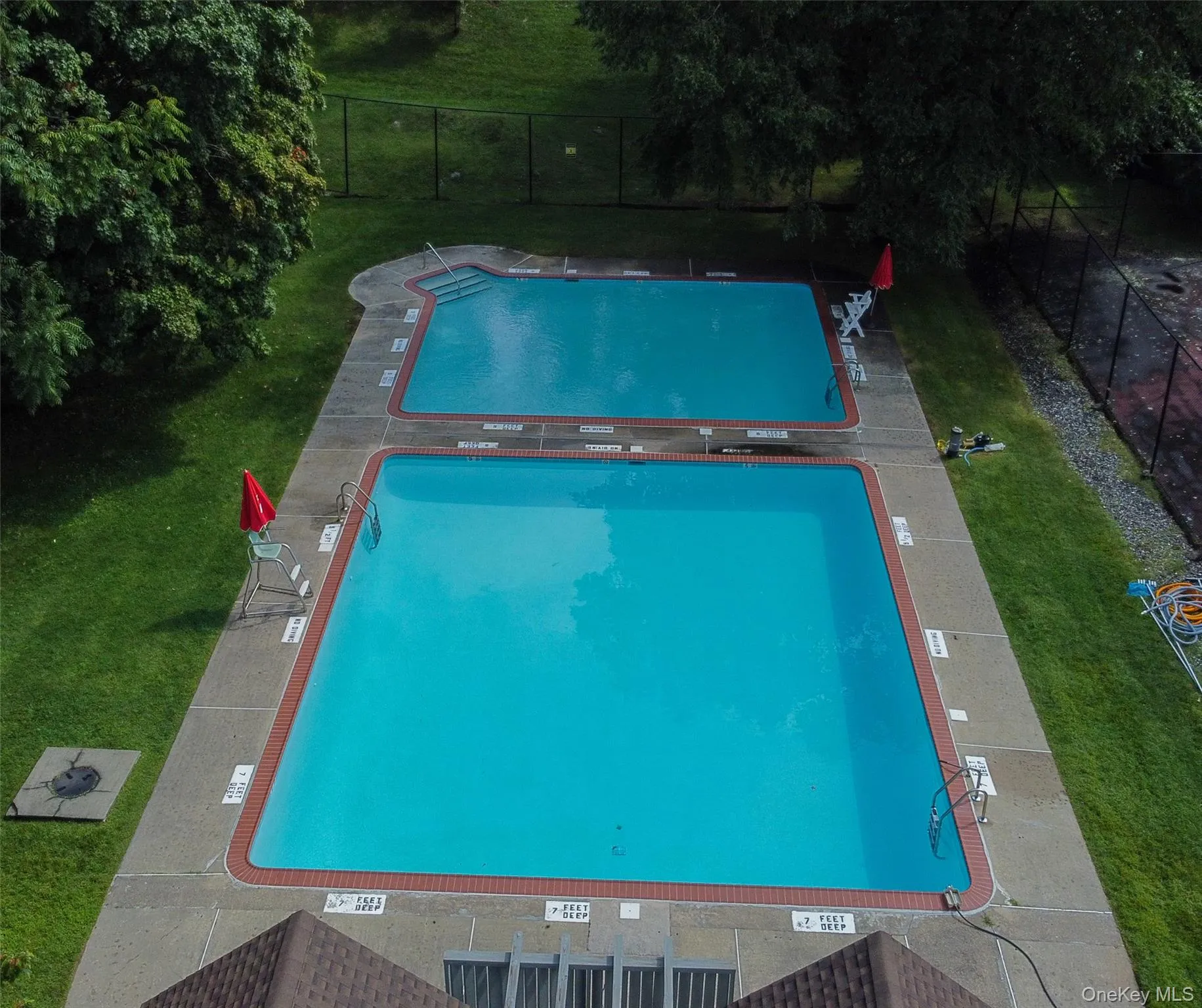 Two outdoor swimming pools surrounded by mature trees and green space. Two outdoor swimming pools surrounded by mature trees and green space.