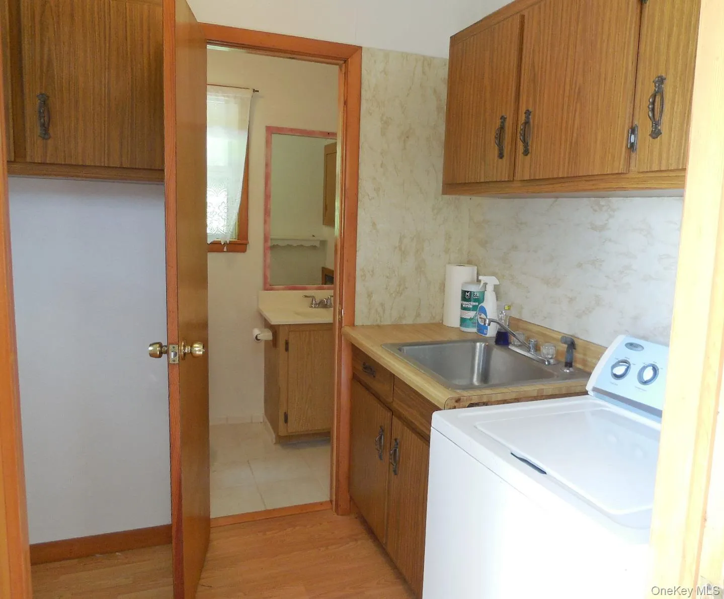 Laundry area featuring wood-finish flooring, a stainless steel utility sink, and wood-finish cabinetry Laundry area featuring wood-finish flooring, a stainless steel utility sink, and wood-finish cabinetry