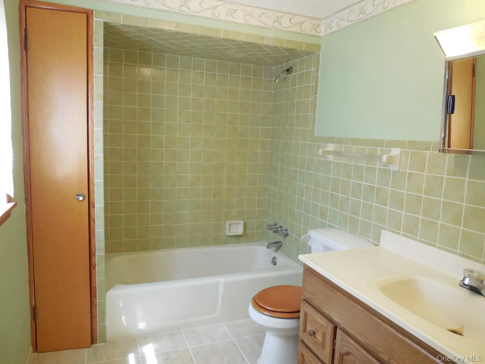 Full bathroom featuring a single vanity with wood-finish cabinetry, a white porcelain sink, a toilet, and a bathtub with a shower Full bathroom featuring a single vanity with wood-finish cabinetry, a white porcelain sink, a toilet, and a bathtub with a shower