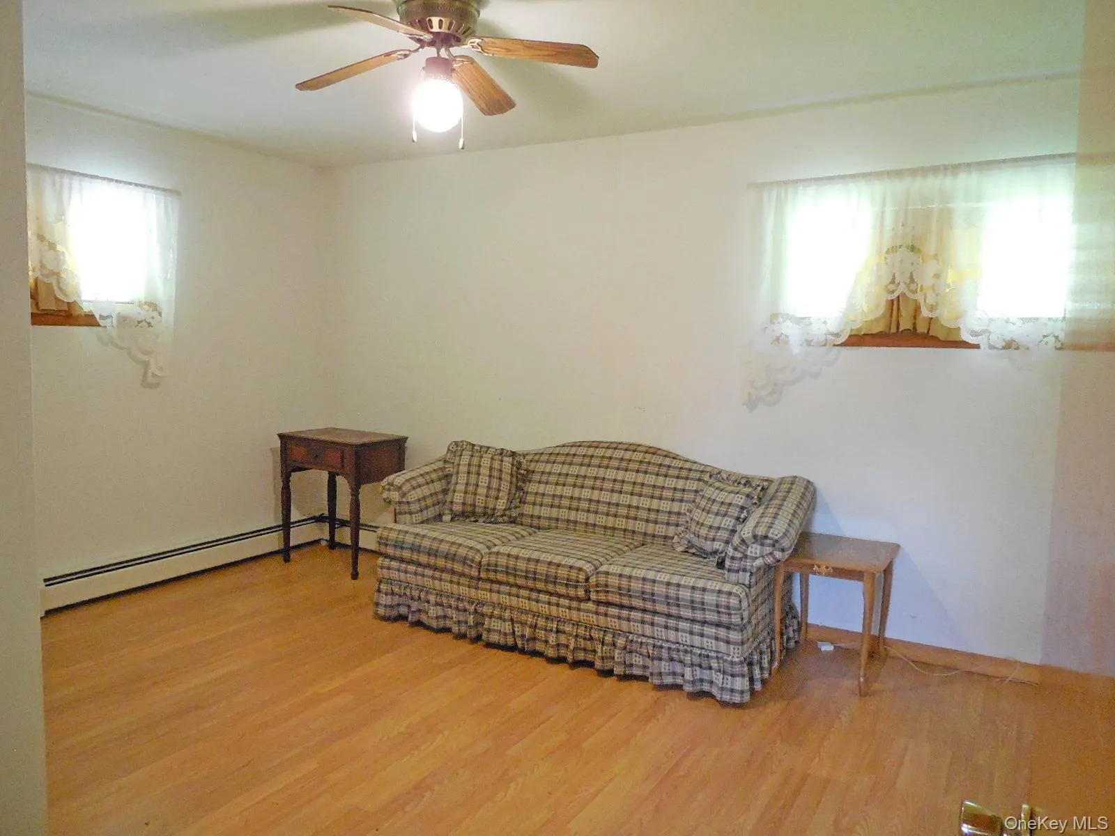Wood-finish flooring, ceiling fan with light fixture, window with wood trim, and baseboard heating Wood-finish flooring, ceiling fan with light fixture, window with wood trim, and baseboard heating
