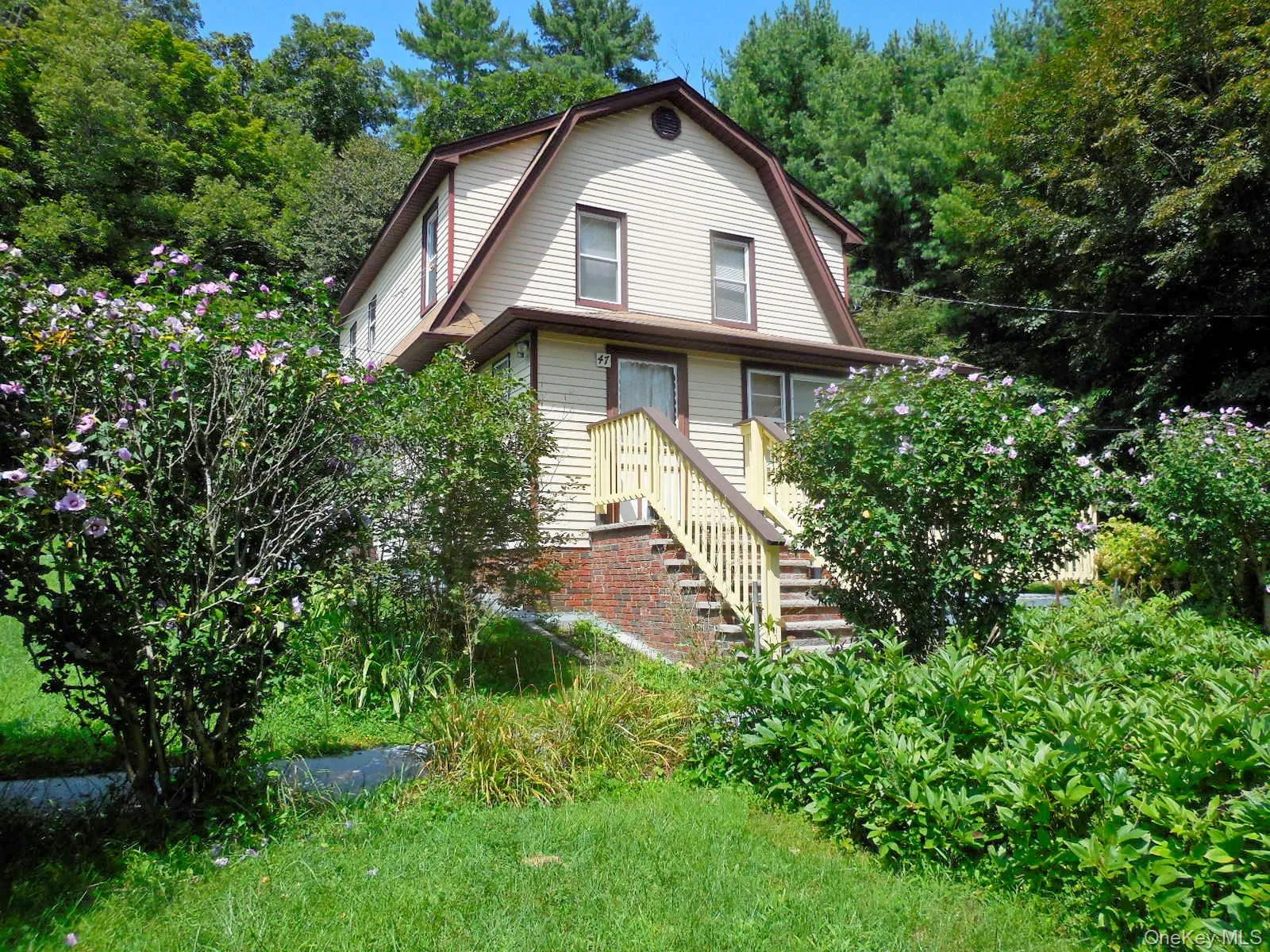 Gambrel roofline with dormer windows, elevated entry with staircase and mature landscaping Gambrel roofline with dormer windows, elevated entry with staircase and mature landscaping
