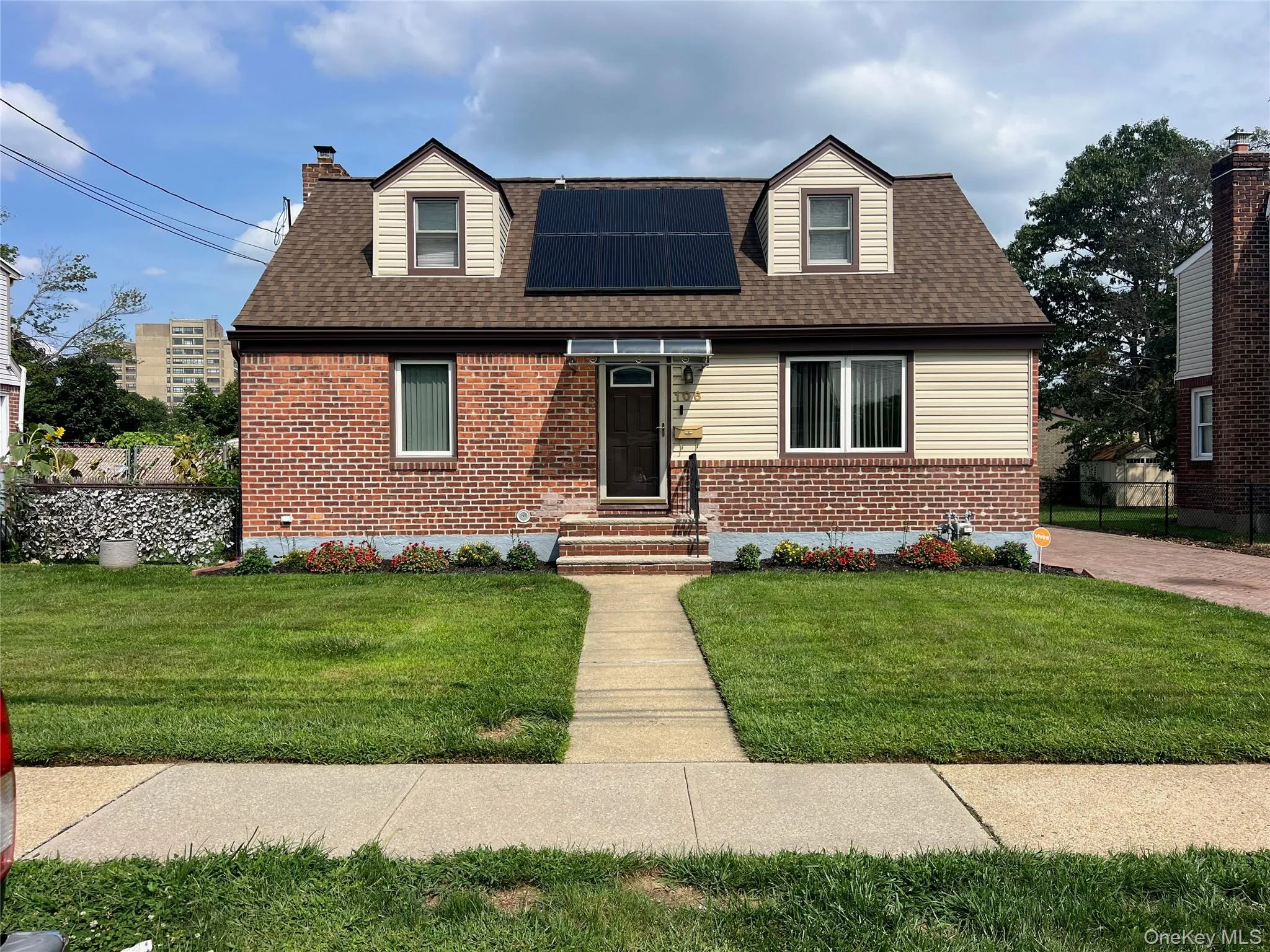 Brick and siding exterior with a pitched shingle roof, dormer windows, and a concrete walkway Brick and siding exterior with a pitched shingle roof, dormer windows, and a concrete walkway