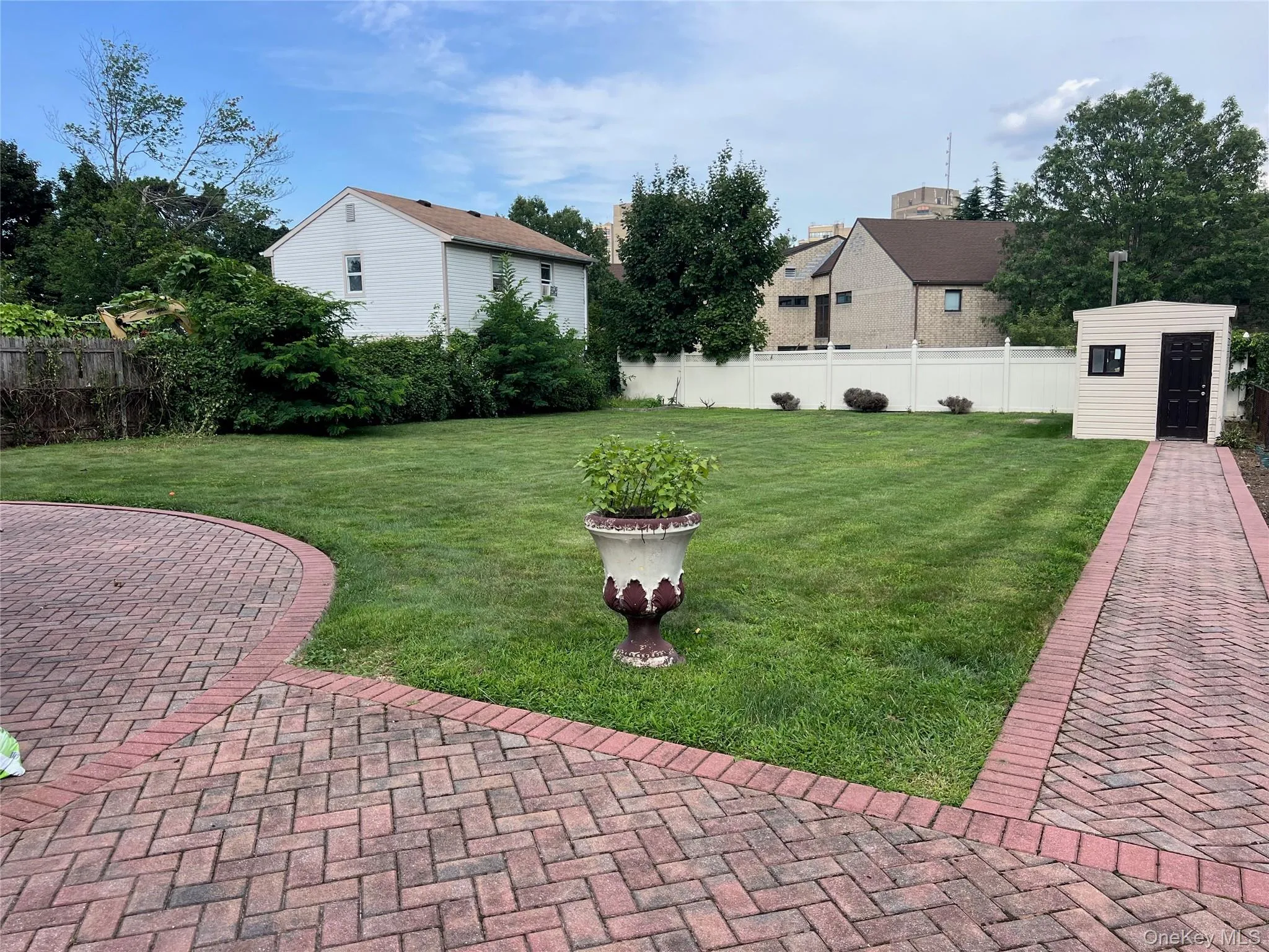 Expansive lawn with a paver patio and walkway, featuring a white privacy fence and a detached storage shed Expansive lawn with a paver patio and walkway, featuring a white privacy fence and a detached storage shed