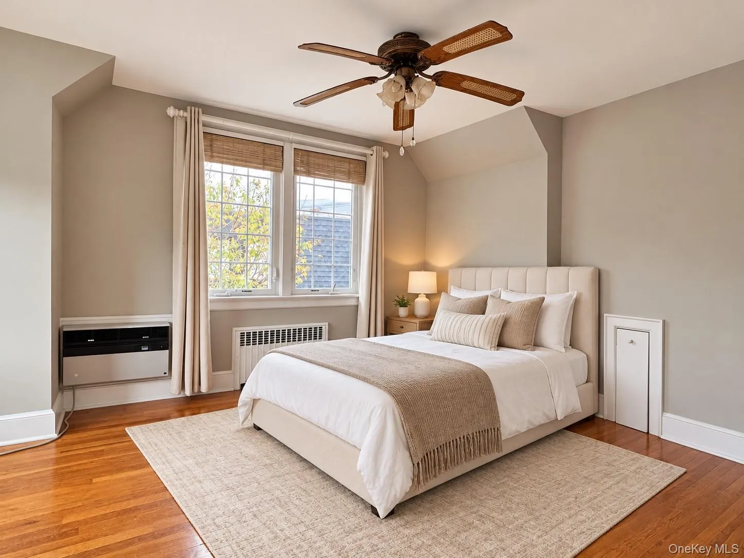 Hardwood flooring, multi-pane windows with integrated wooden blinds, a ceiling fan with integrated lighting, and a wall-mounted climate control unit Hardwood flooring, multi-pane windows with integrated wooden blinds, a ceiling fan with integrated lighting, and a wall-mounted climate control unit