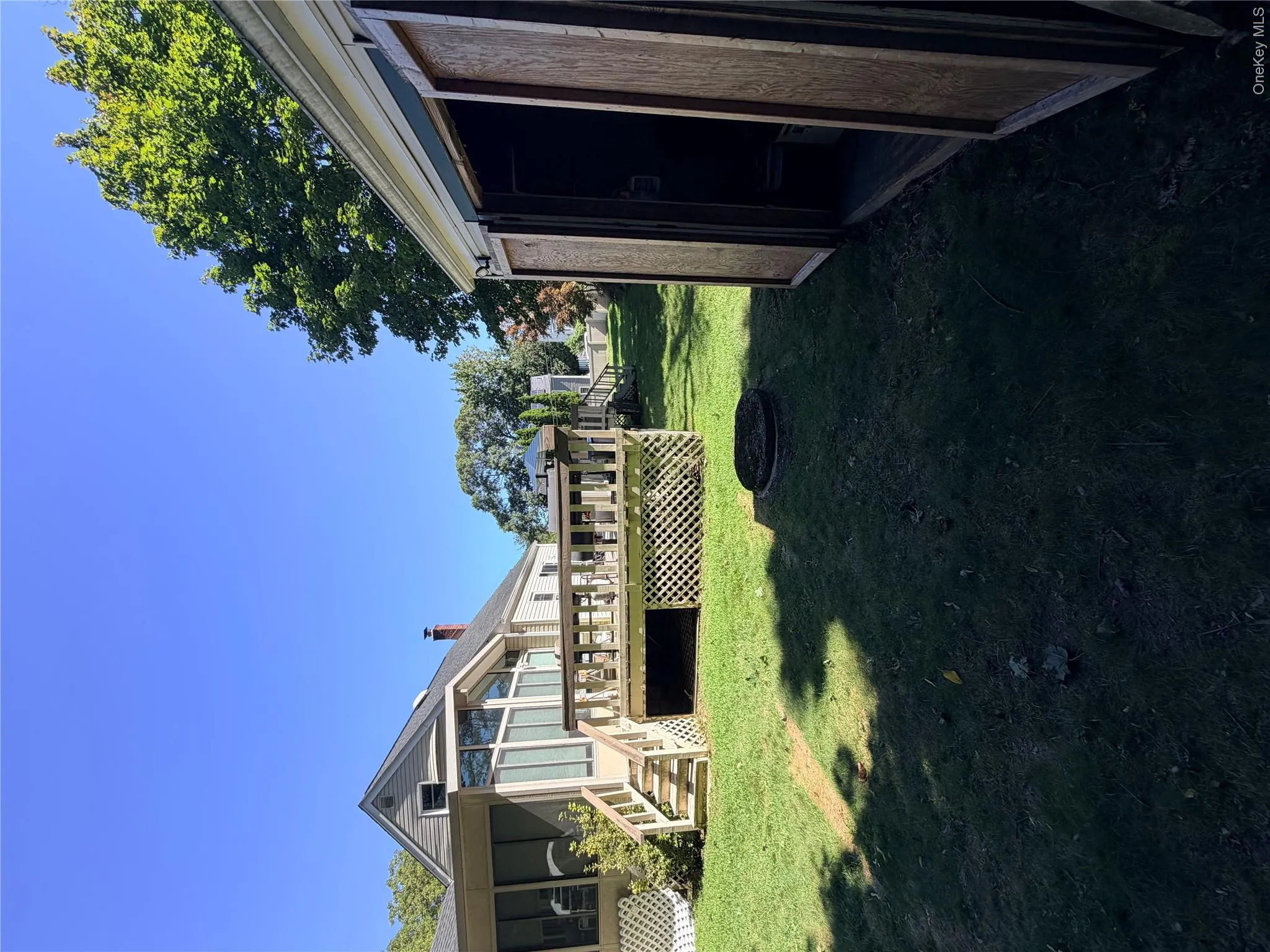 Expansive green lawn with a wooden deck featuring lattice skirting, steps, and a railing Expansive green lawn with a wooden deck featuring lattice skirting, steps, and a railing