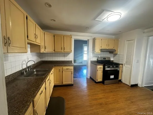 Kitchen featuring a double basin stainless steel sink, light-toned cabinetry, tile backsplash, and wood-finish flooring Kitchen featuring a double basin stainless steel sink, light-toned cabinetry, tile backsplash, and wood-finish flooring